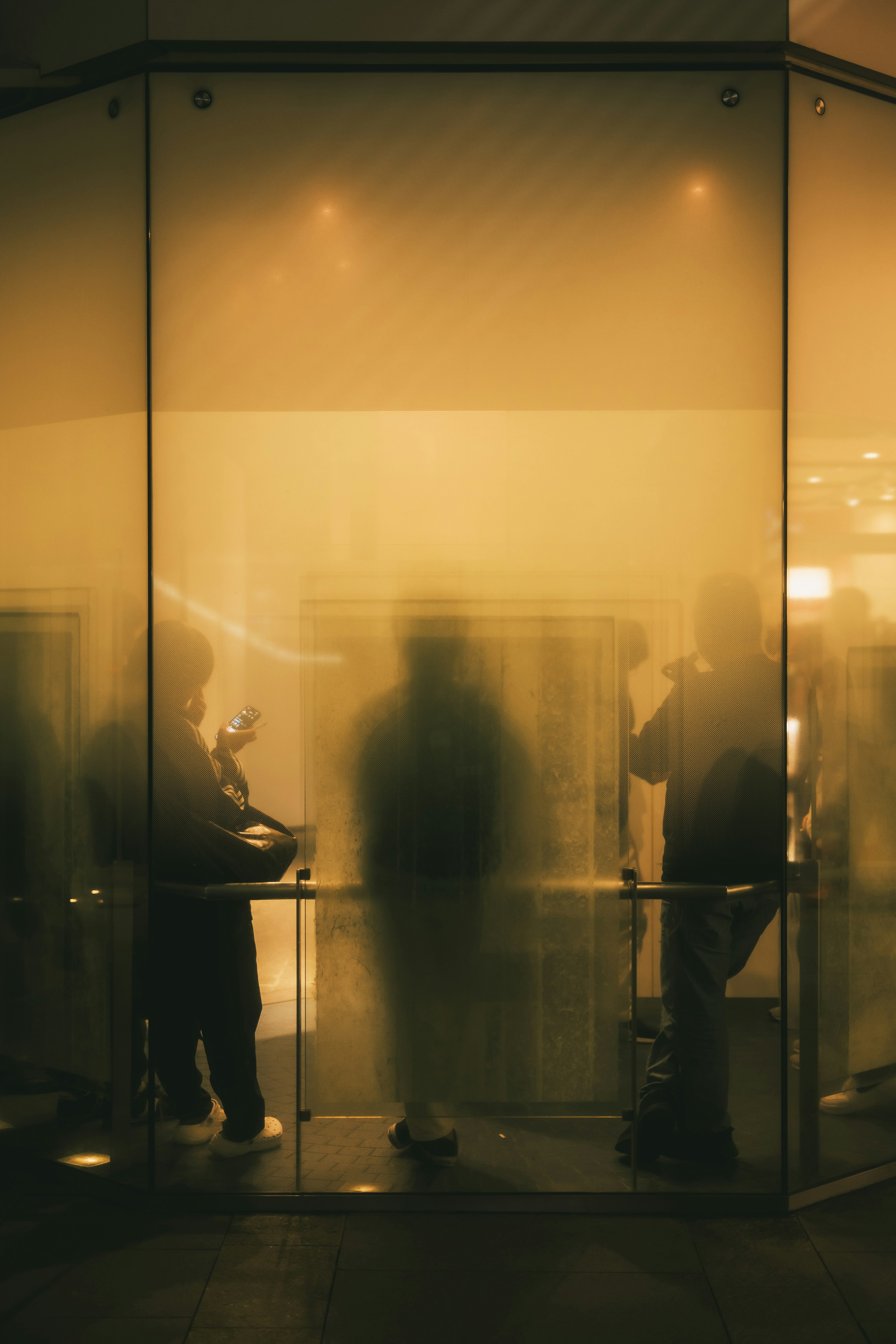 Silhouettes of people inside a glass structure illuminated by yellow light