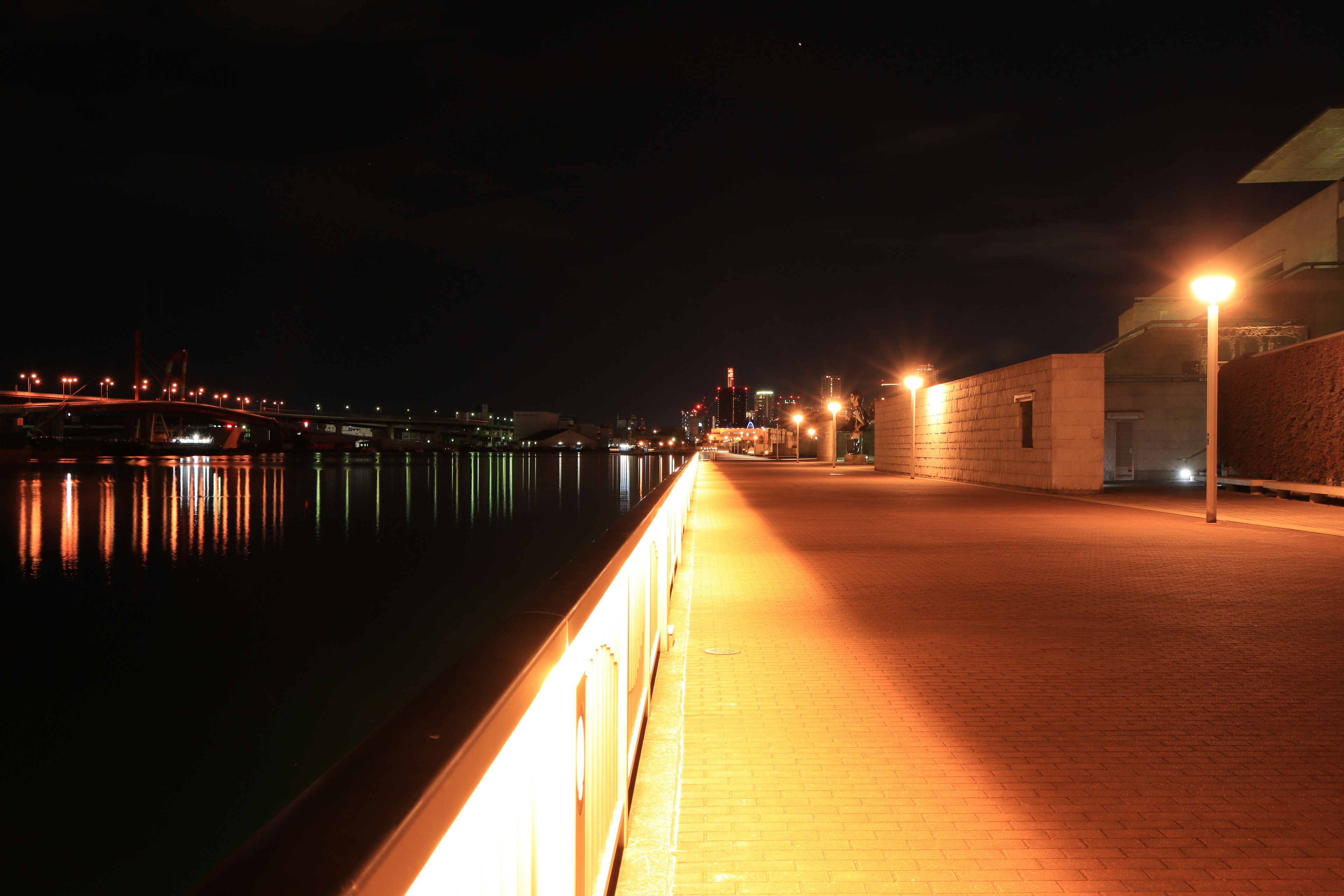 Quiet riverside walkway at night illuminated by streetlights