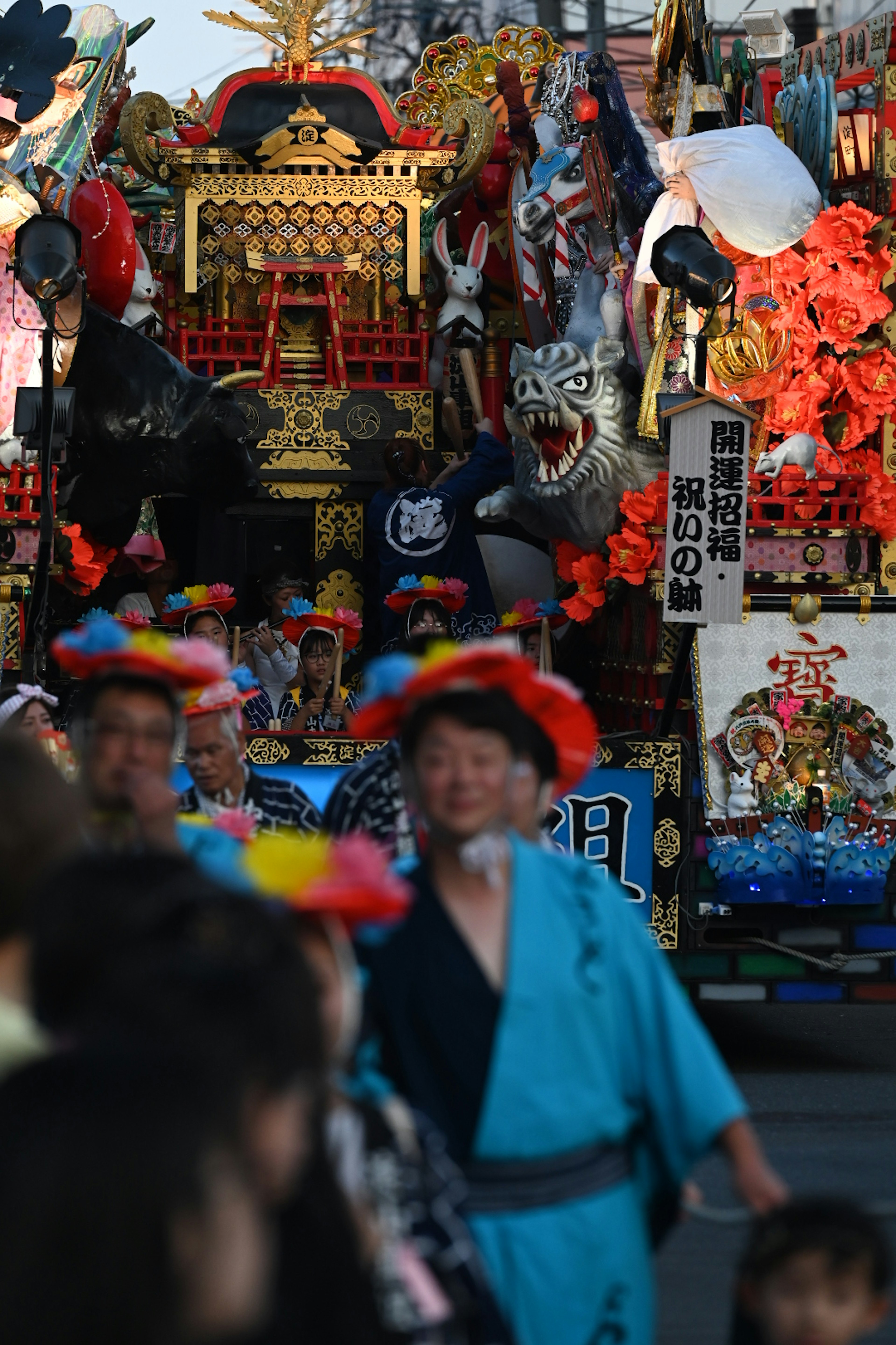 祭りのパレードで色鮮やかな衣装を着た人々と装飾された山車が映る