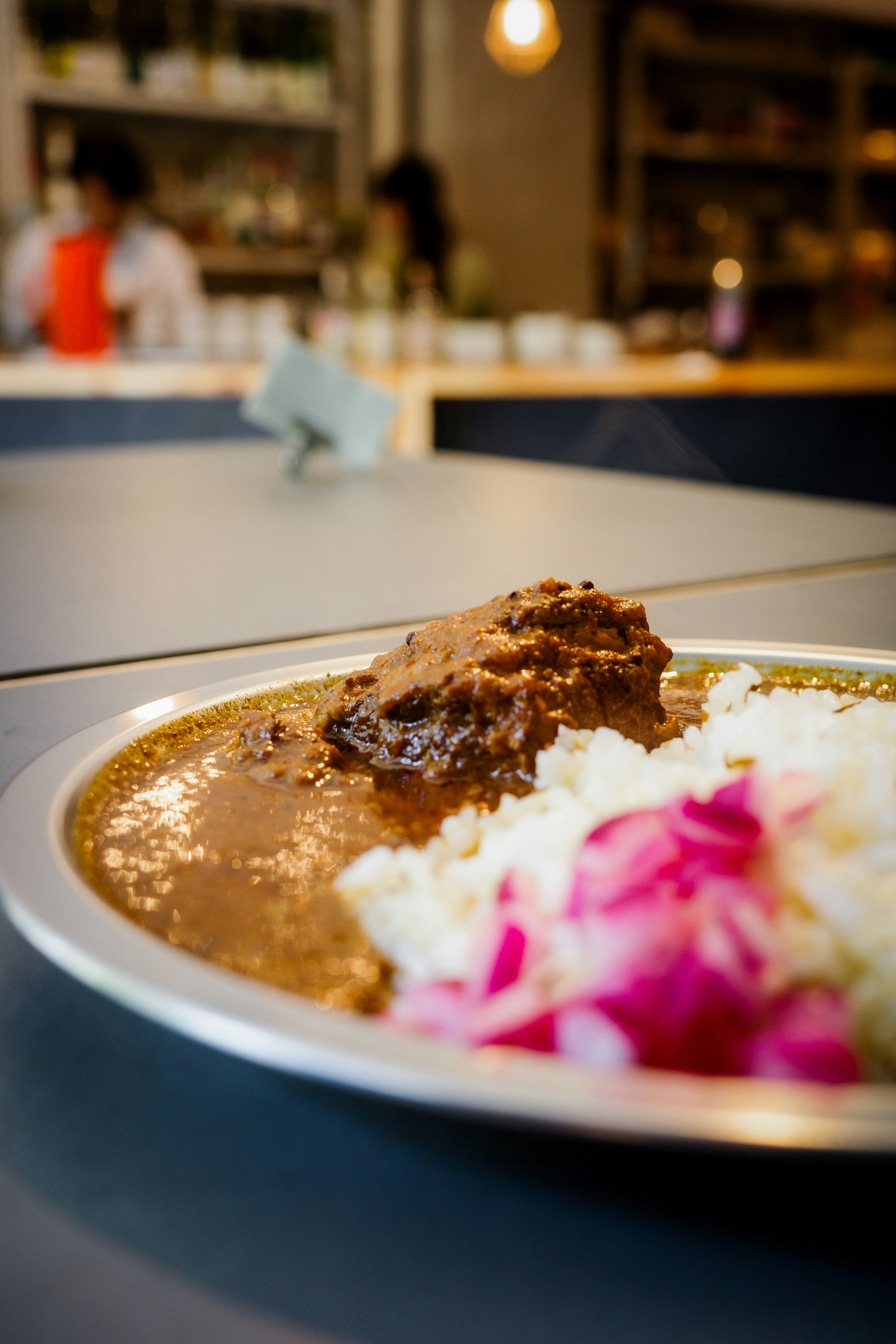 A close-up of a plate with curry and rice garnished with pink flowers out of focus people in the background