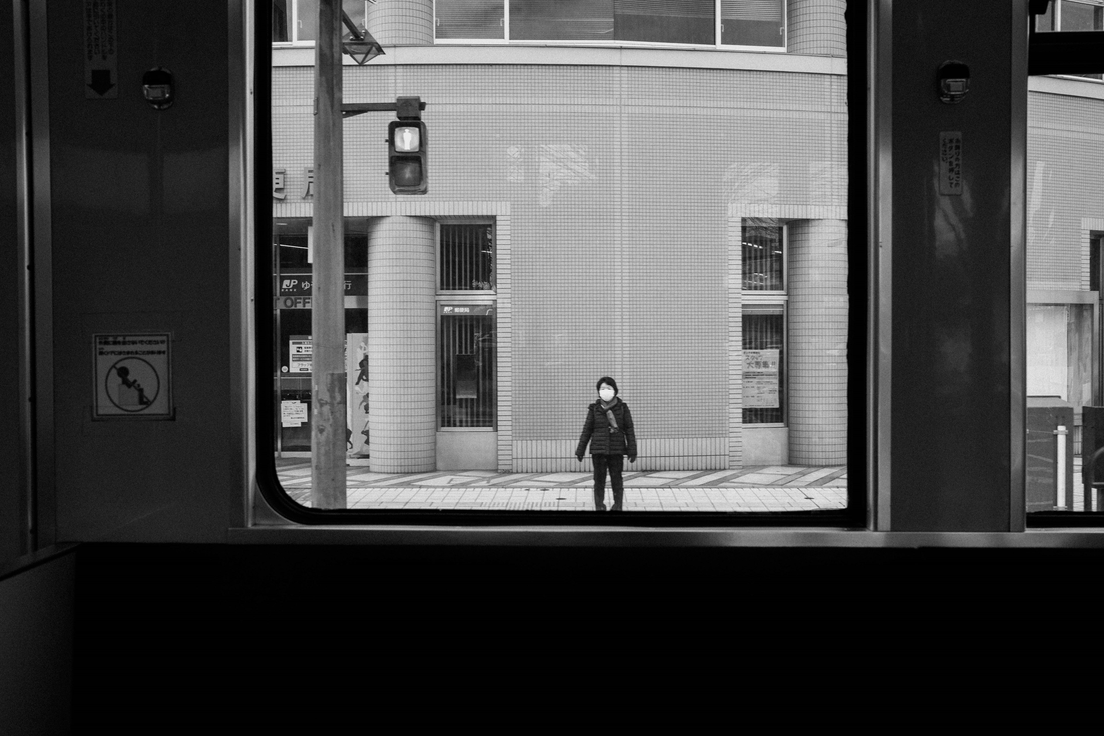 Una persona de pie frente a un edificio vista a través de una ventana de tren