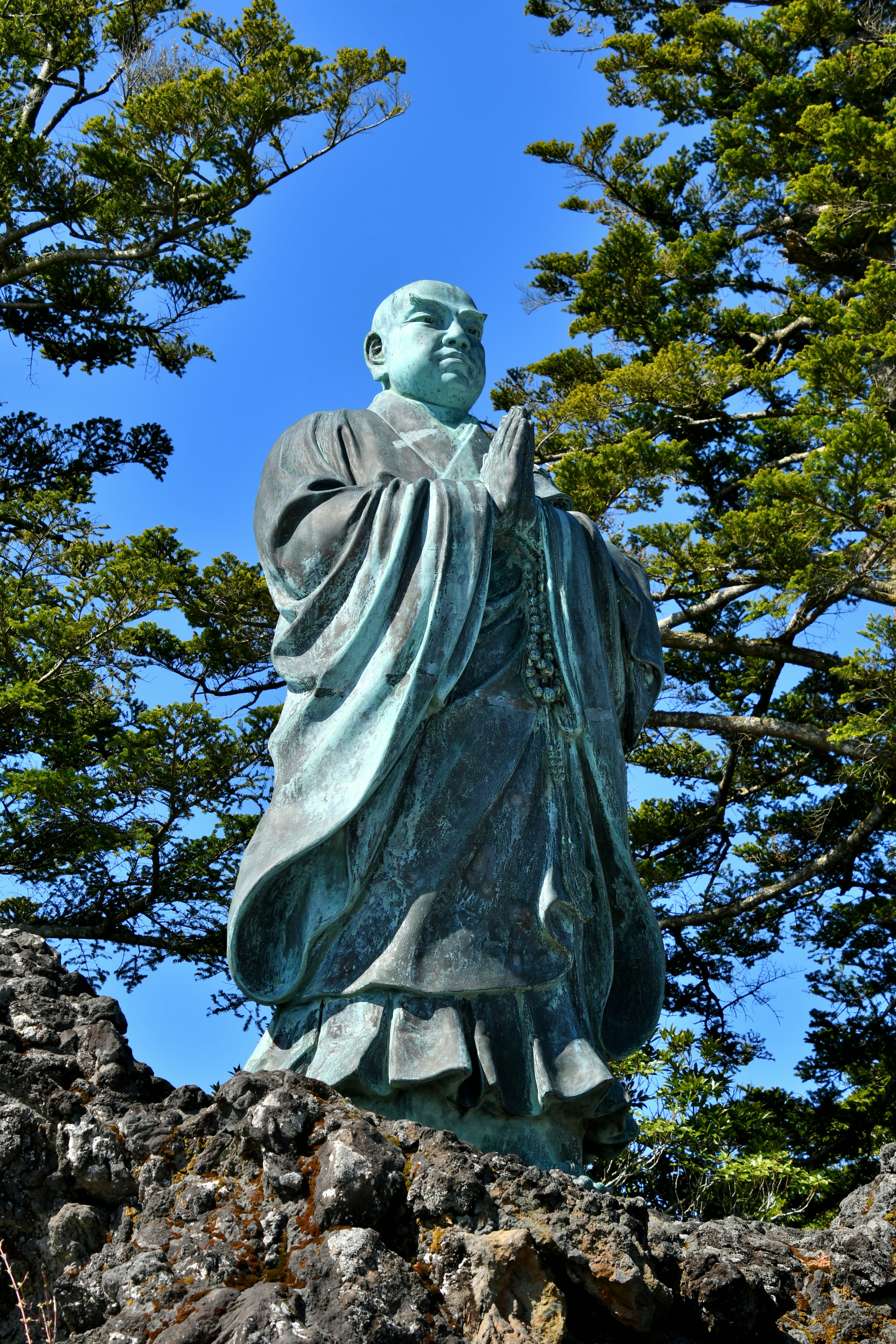 Una estatua de bronce de un monje de pie entre una vegetación exuberante