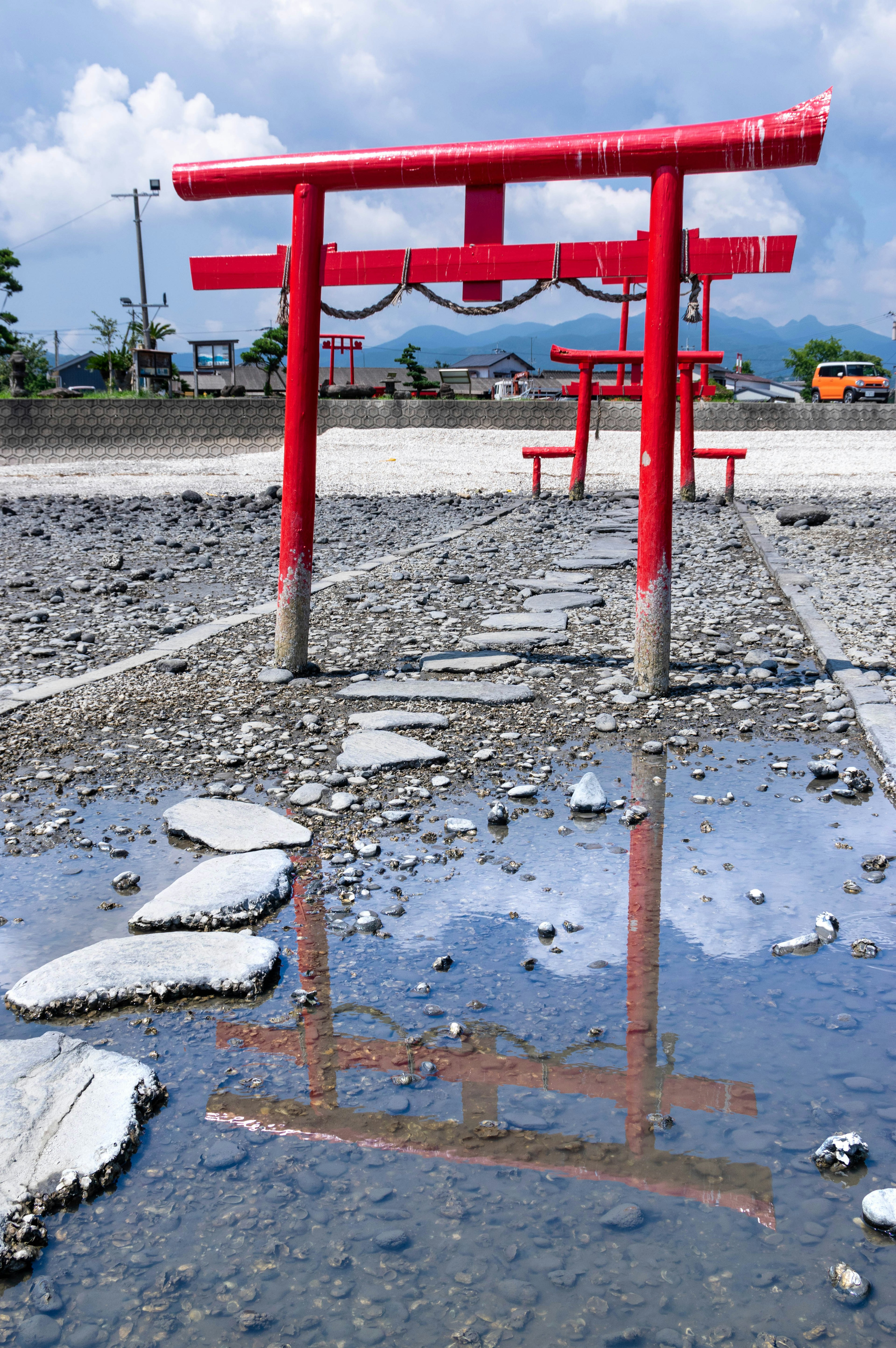 Torii rouge reflété dans une flaque d'eau avec des pierres et un ciel nuageux