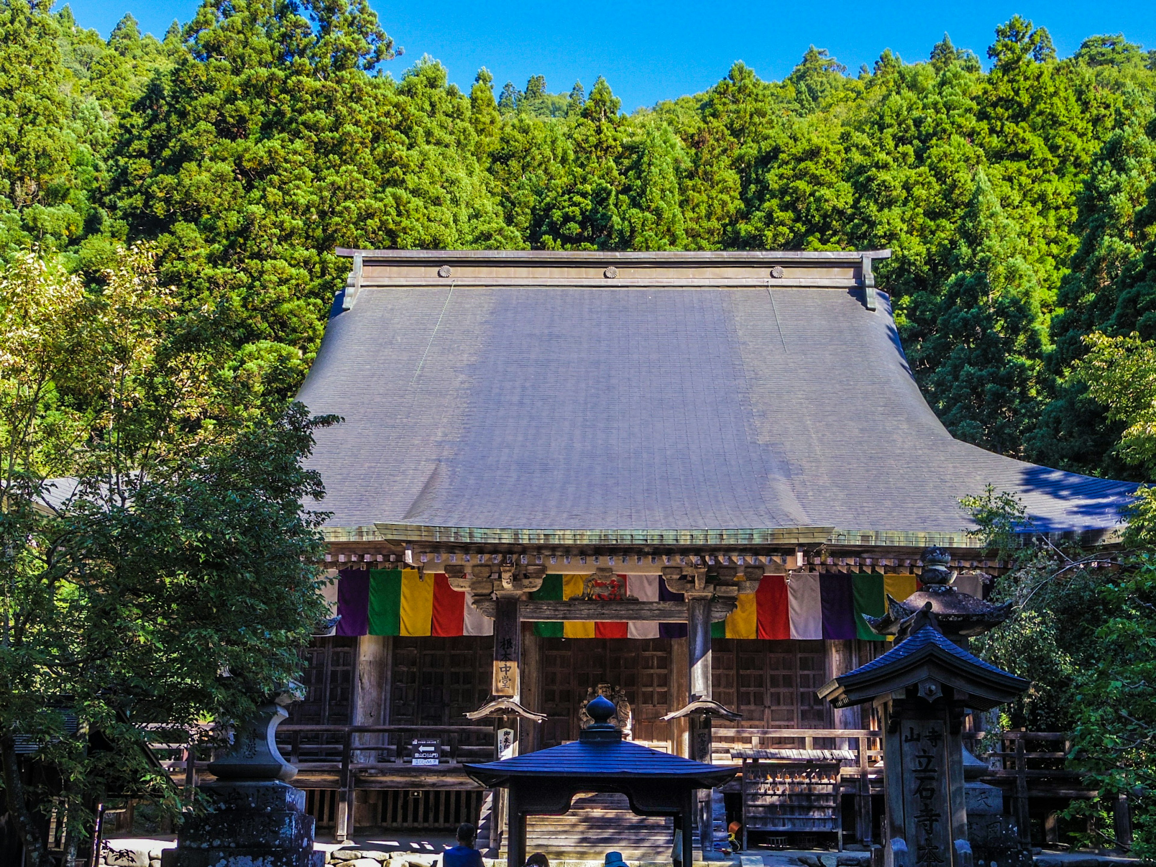 Traditional Japanese temple surrounded by green forest vibrant colored flags displayed