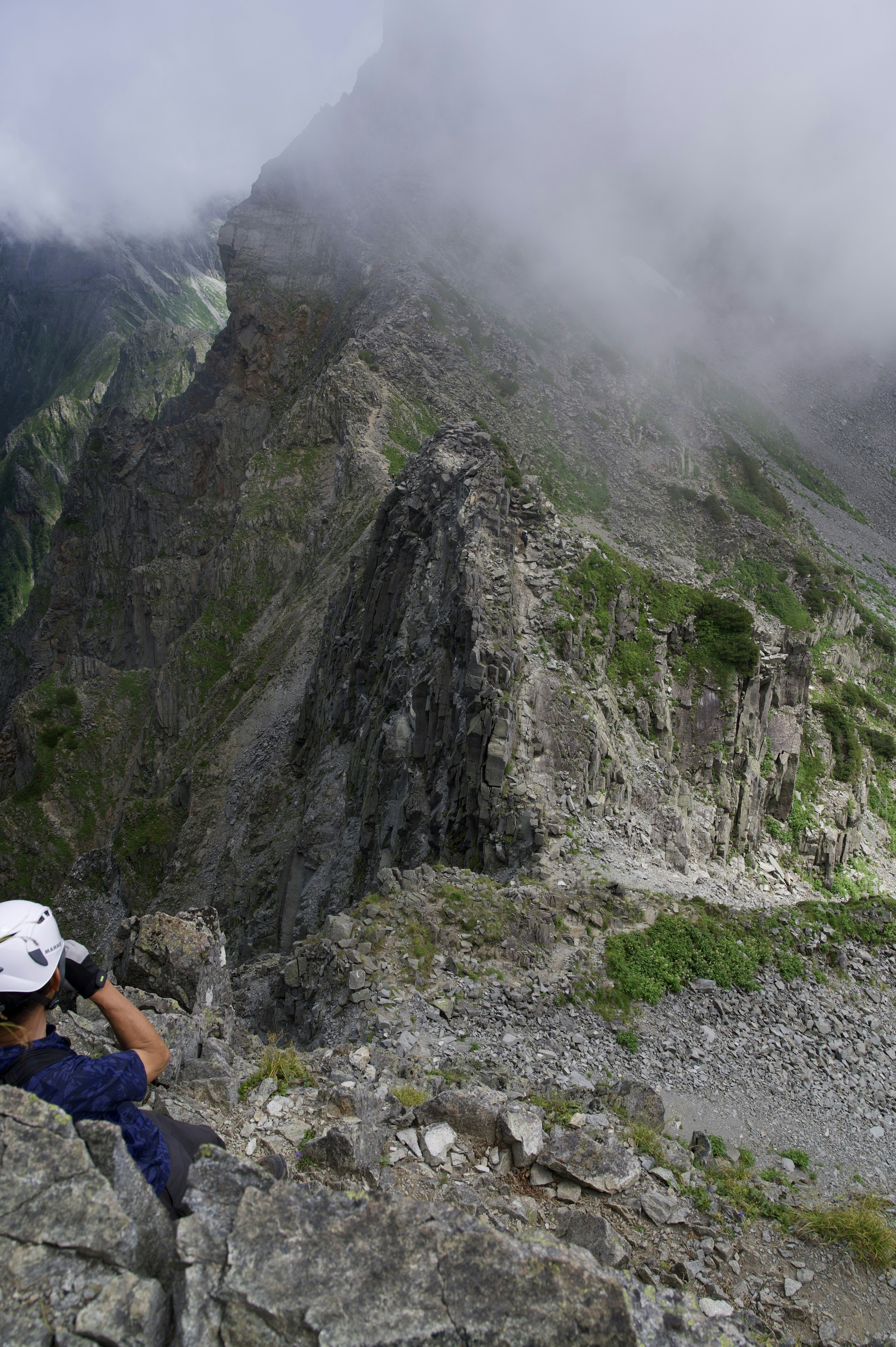 持相机的登山者坐在岩石山峰上，周围被雾气弥漫的山脉包围