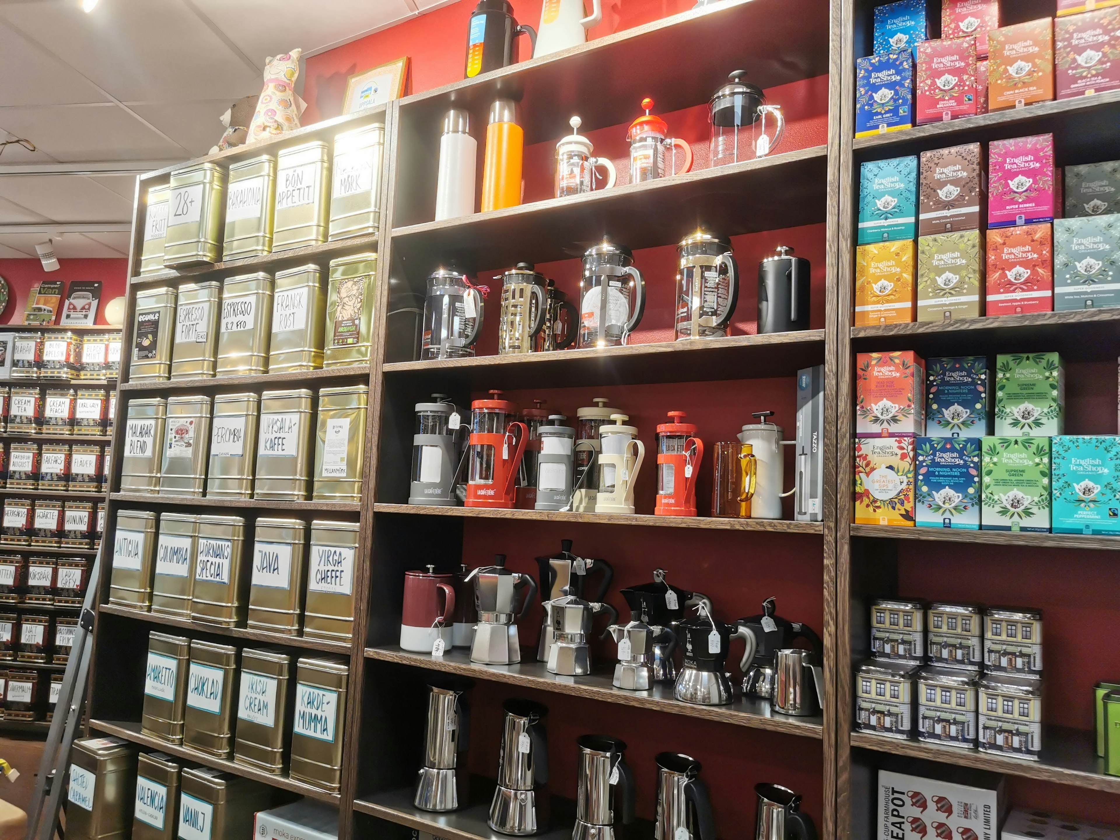 Estantes que exhiben cajas de té y equipo de café contra una pared roja