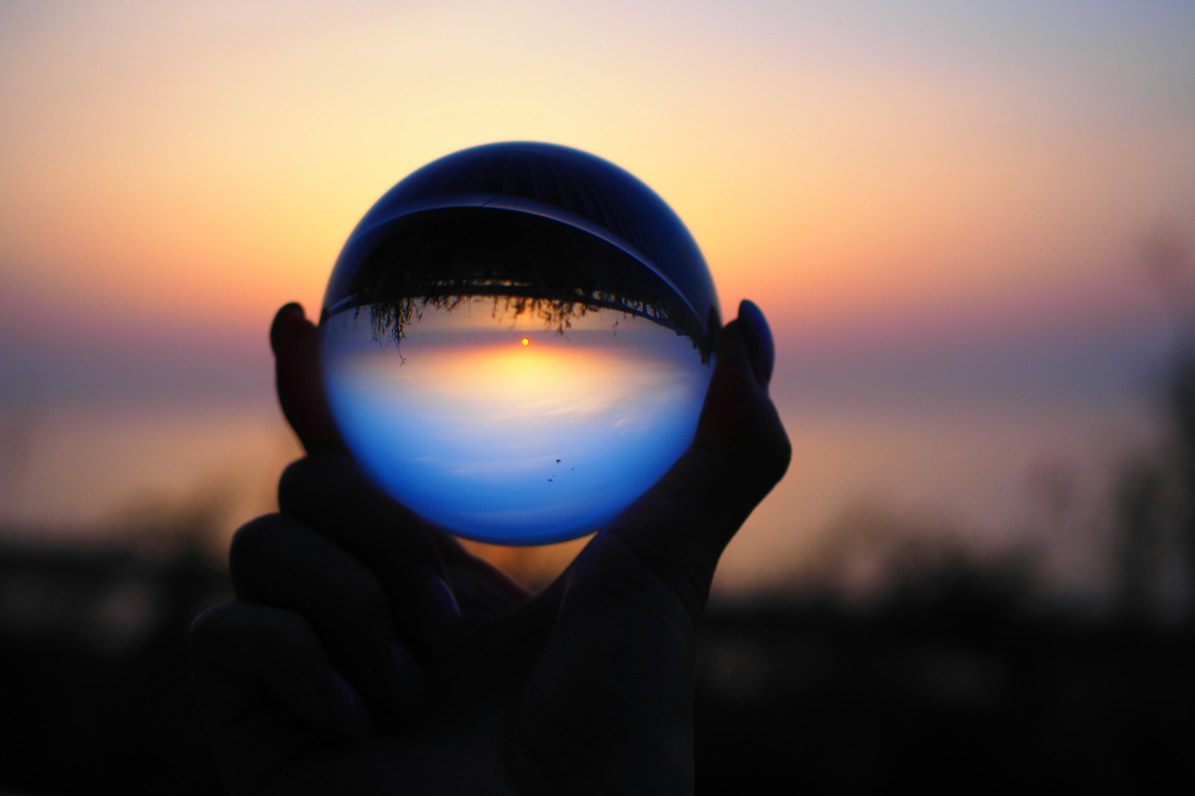 Silueta de una mano sosteniendo una bola de cristal que refleja un atardecer