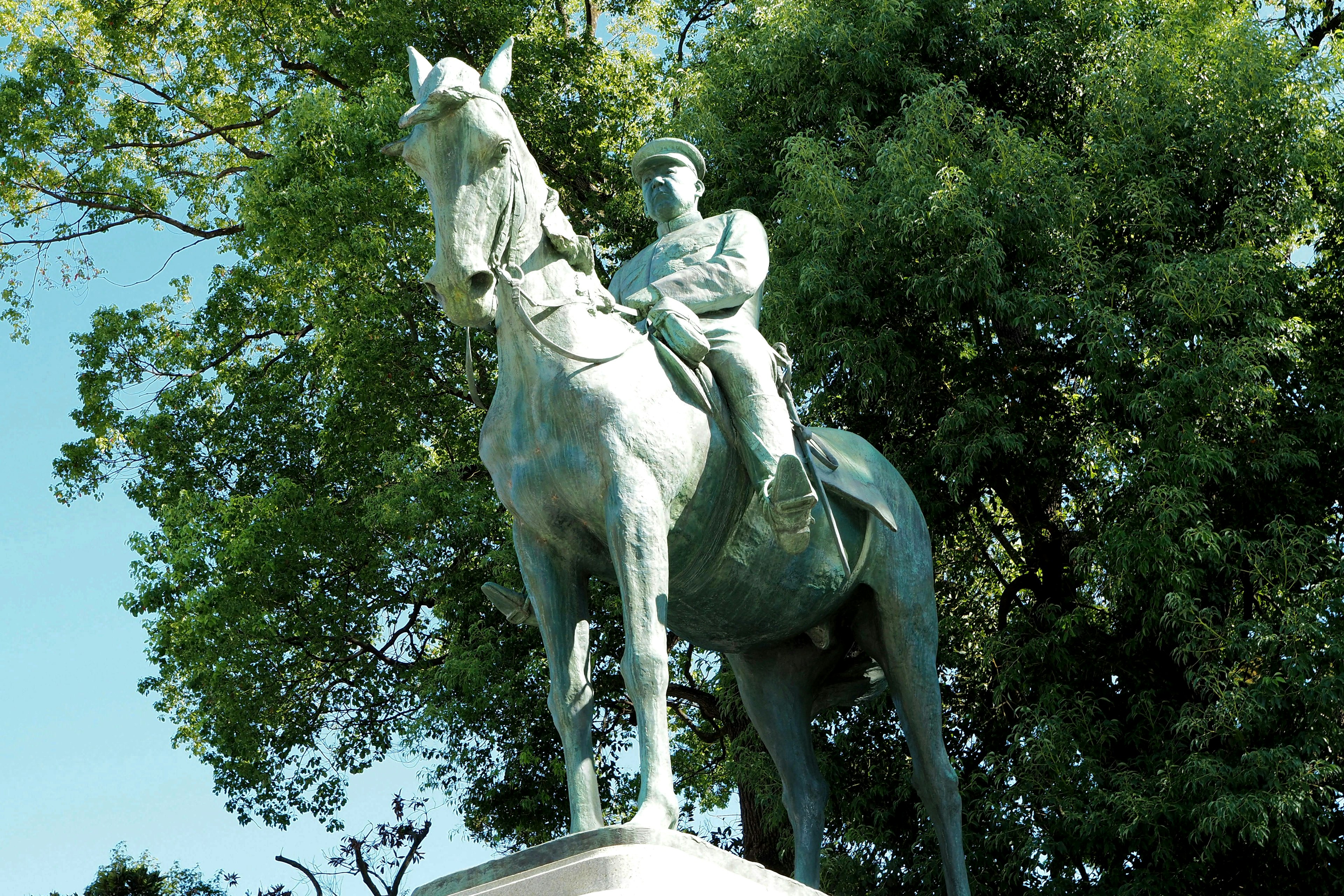 Bronze statue of a soldier on horseback surrounded by lush green trees