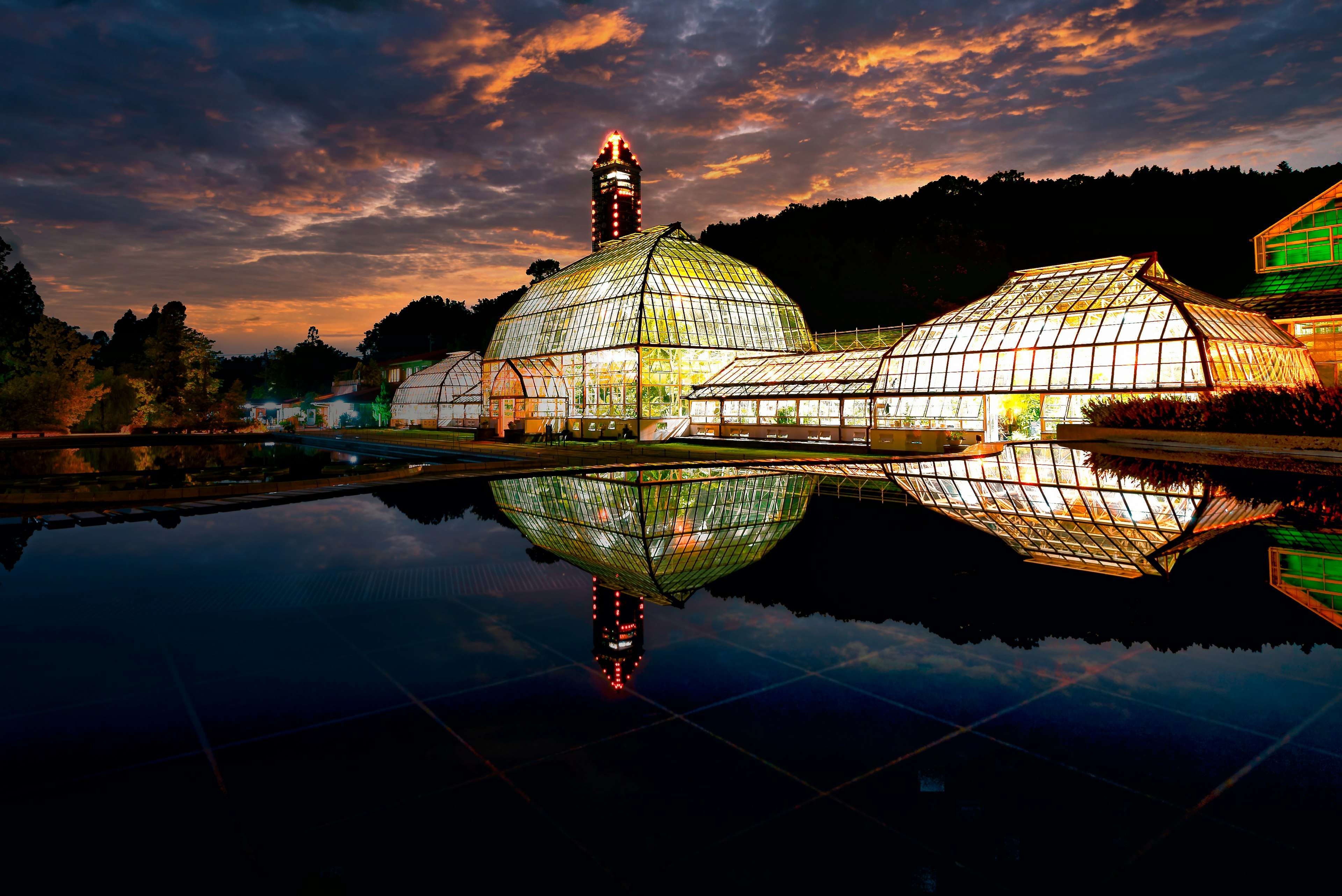 เรือนกระจกสะท้อนในบ่อสงบใต้ท้องฟ้าพระอาทิตย์ตกที่มีสีสัน