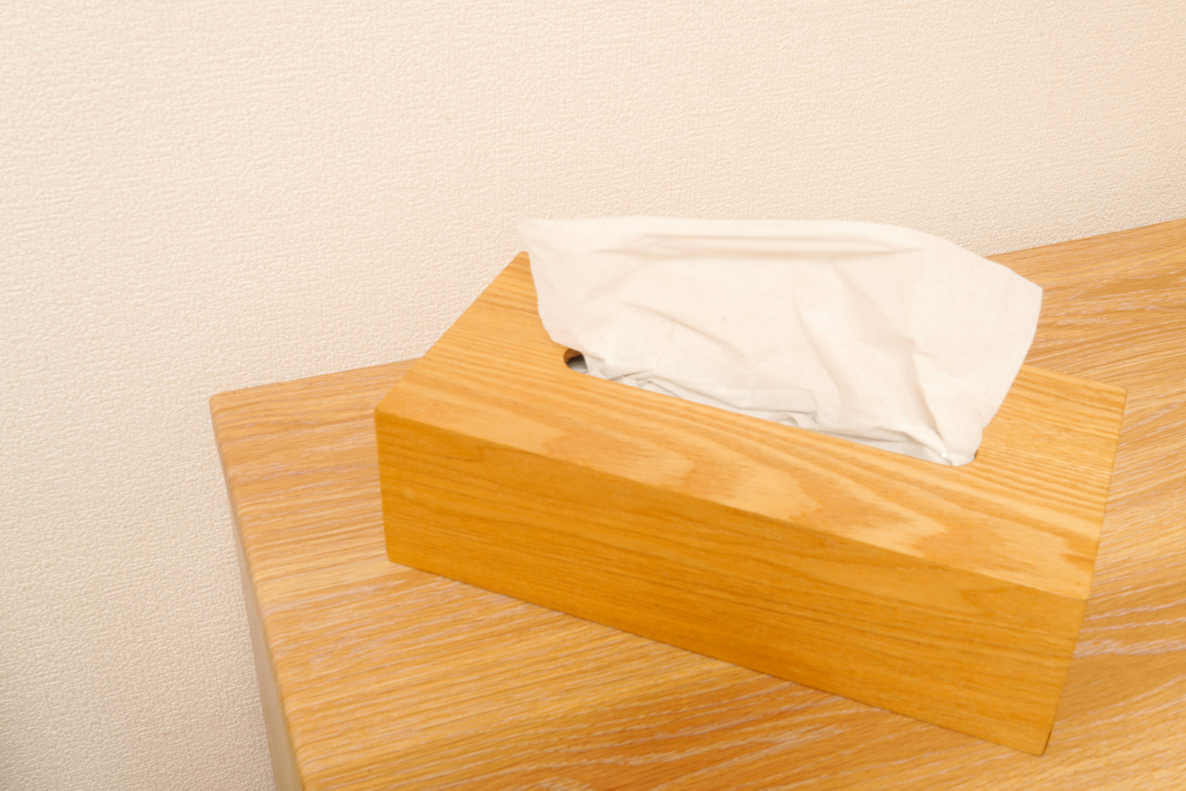 A wooden tissue box with a white tissue on top placed on a light wooden surface