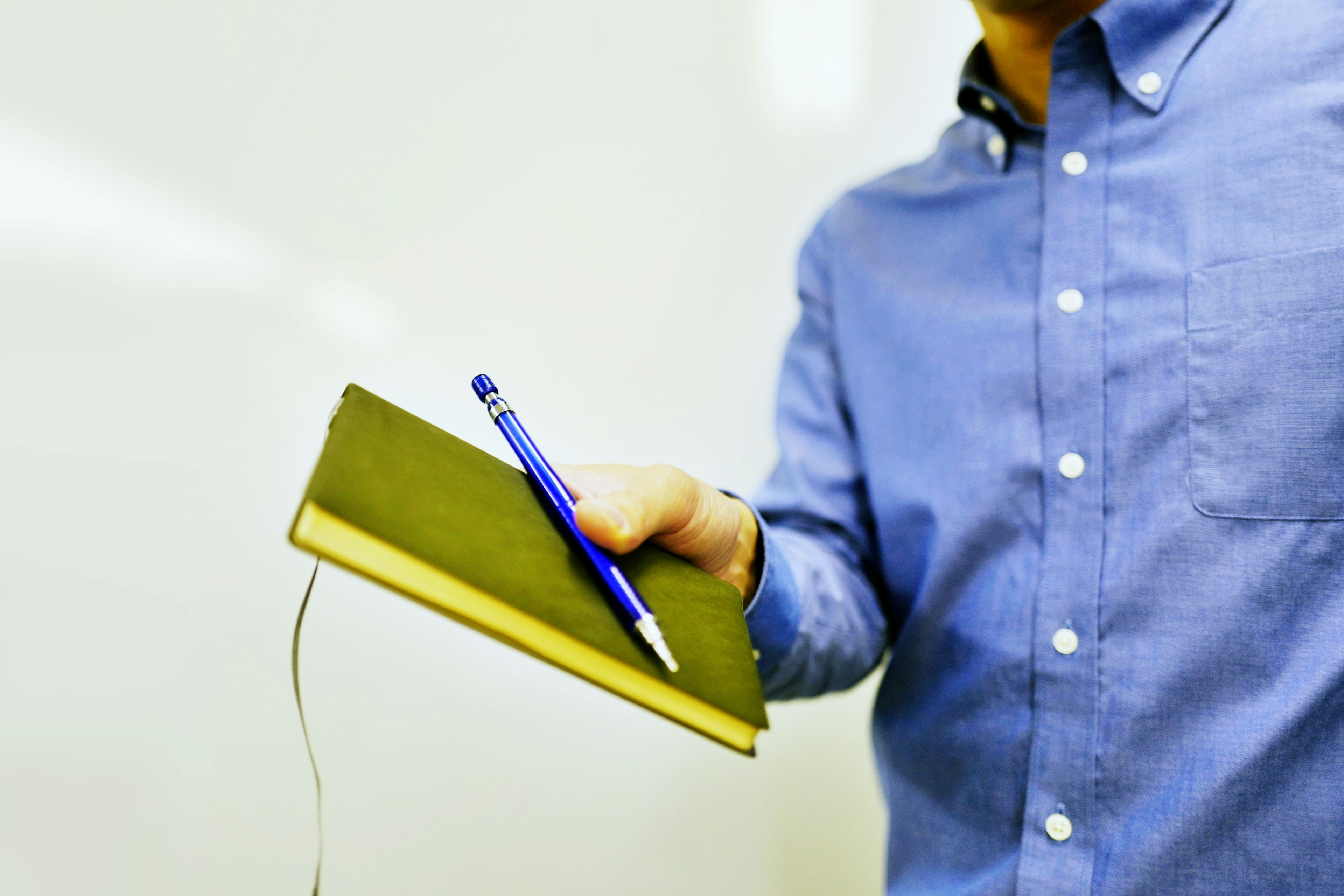 Man in blue shirt holding green notebook and blue pen