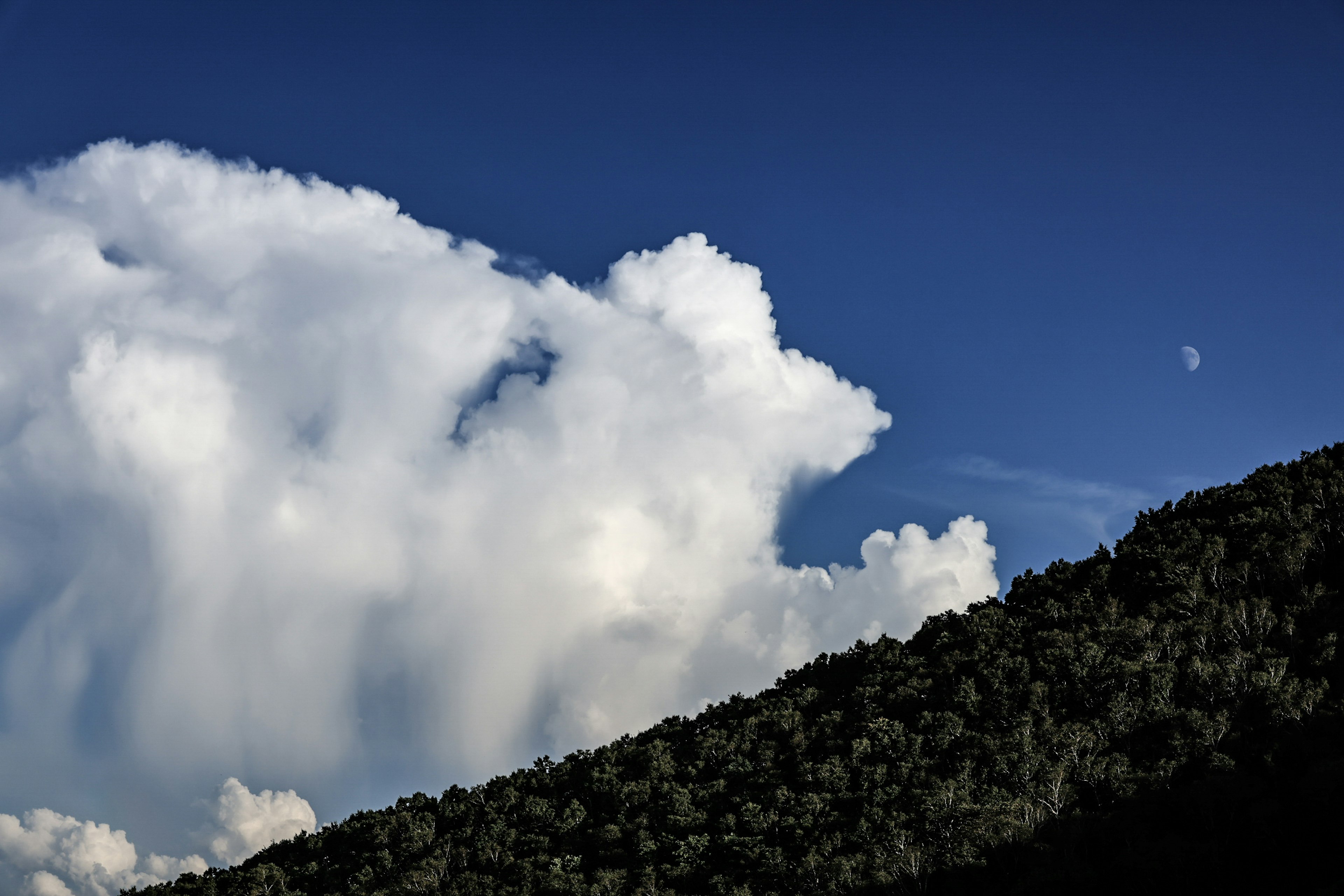 Nubes blancas flotando en un cielo azul sobre la silueta de una montaña verde