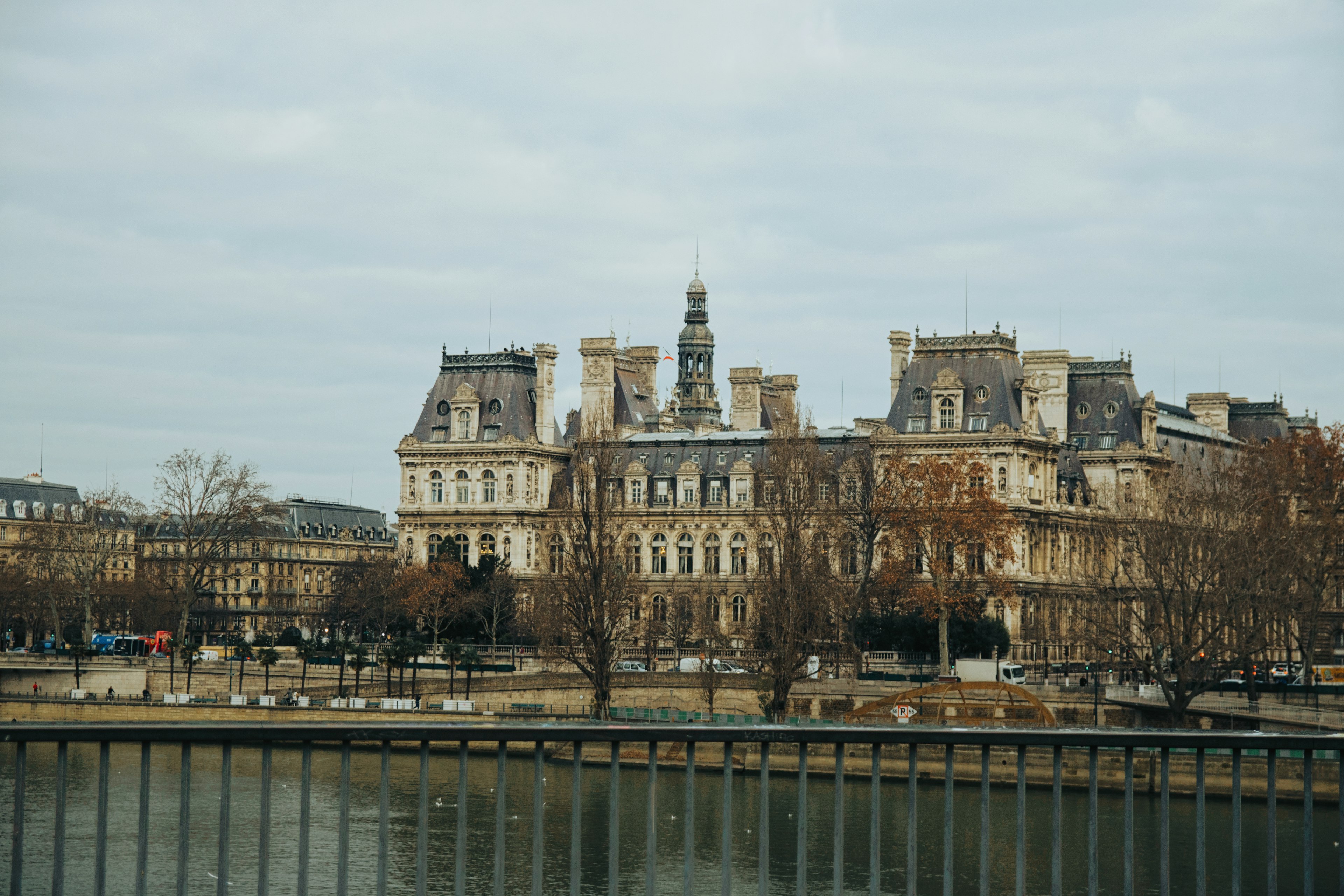 Vista del Ayuntamiento de París mostrando sus detalles arquitectónicos con una superficie de agua tranquila y un cielo gris