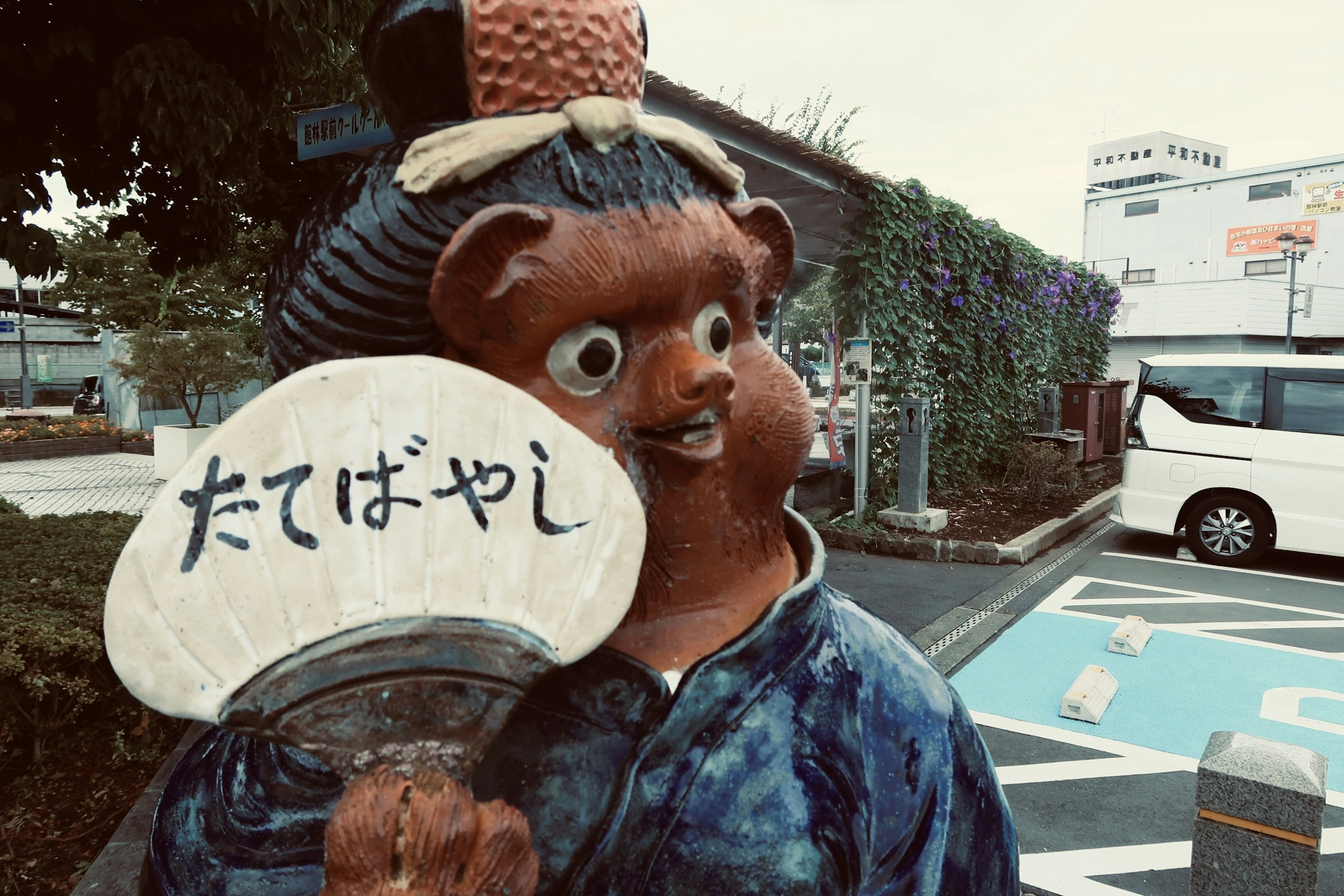 Estatua de oso única que lleva un kimono azul sosteniendo un abanico blanco con texto escrito en japonés