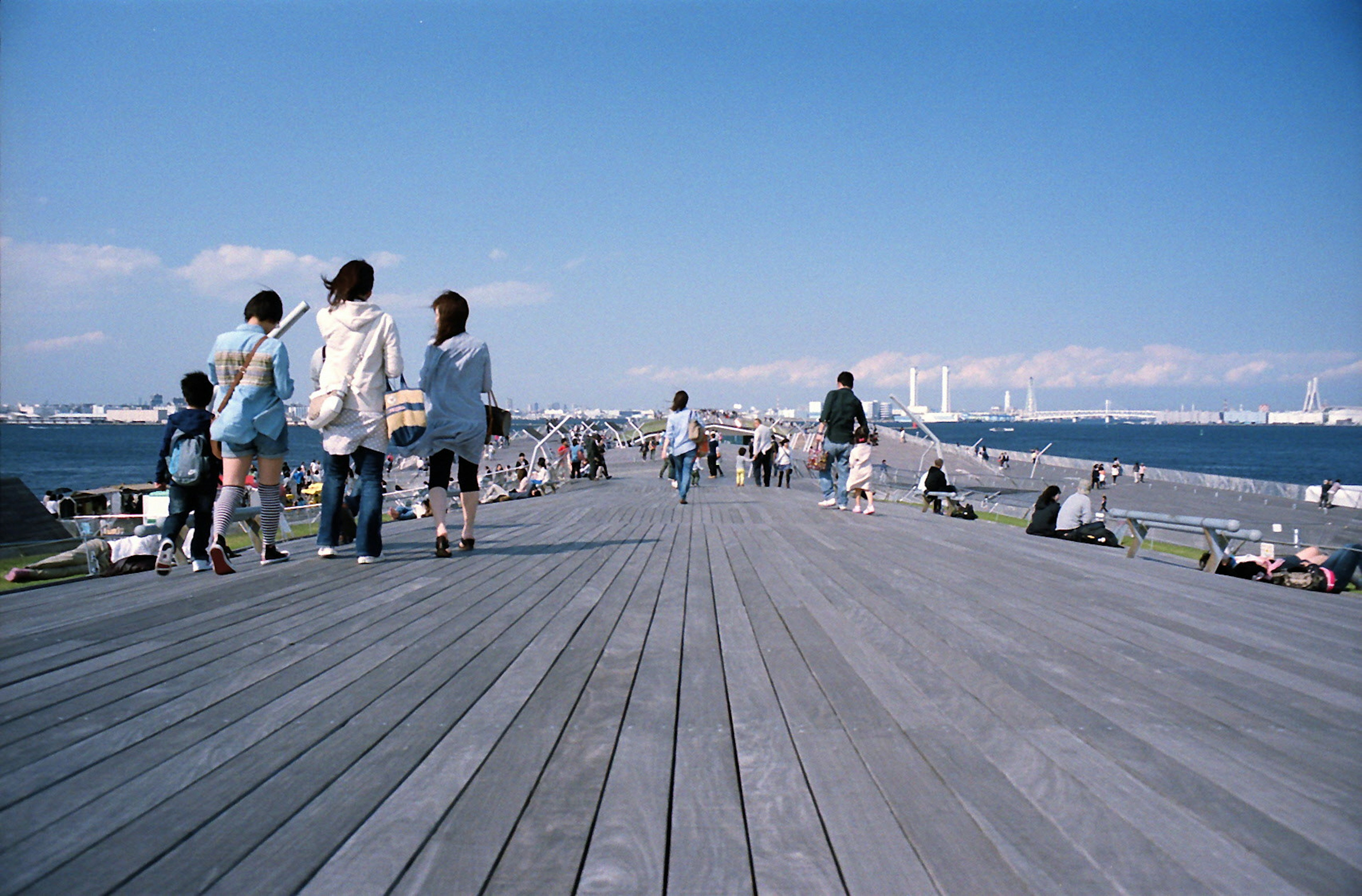 People walking on a wooden pier under a blue sky and ocean