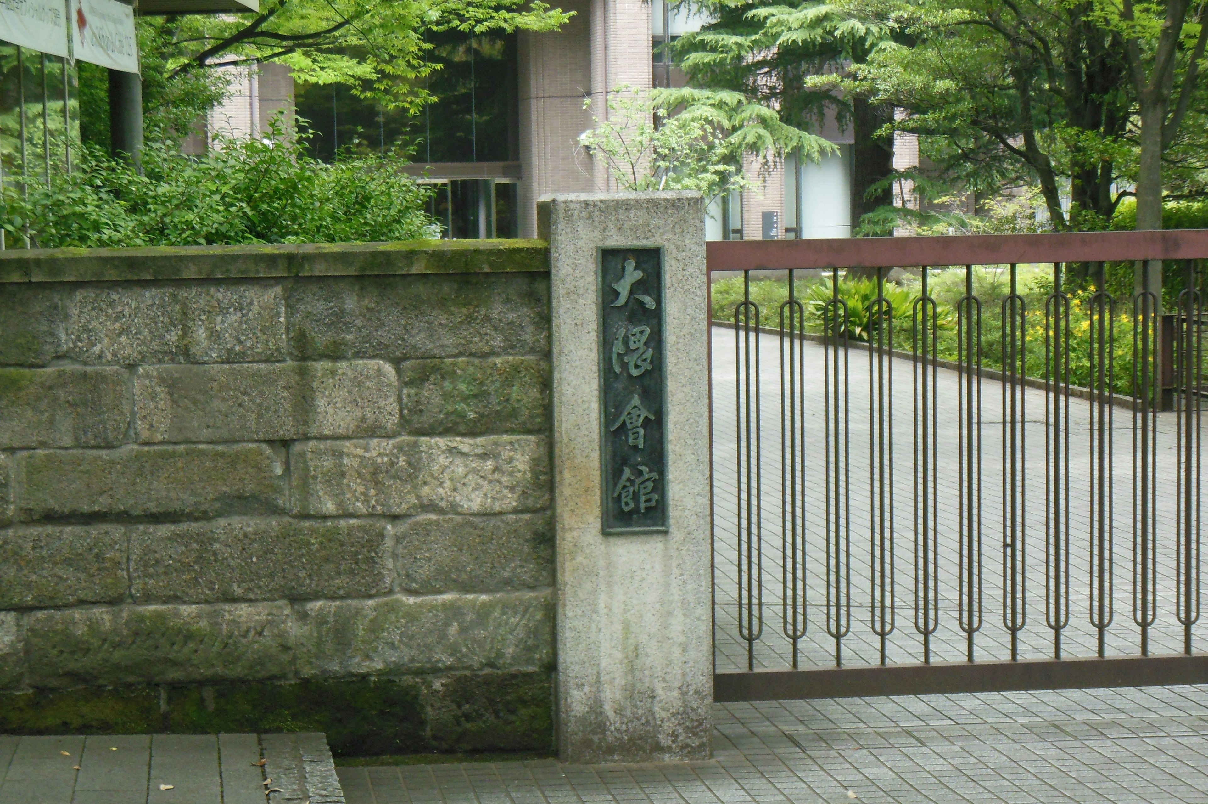 Sign next to a stone wall and iron gate surrounded by greenery