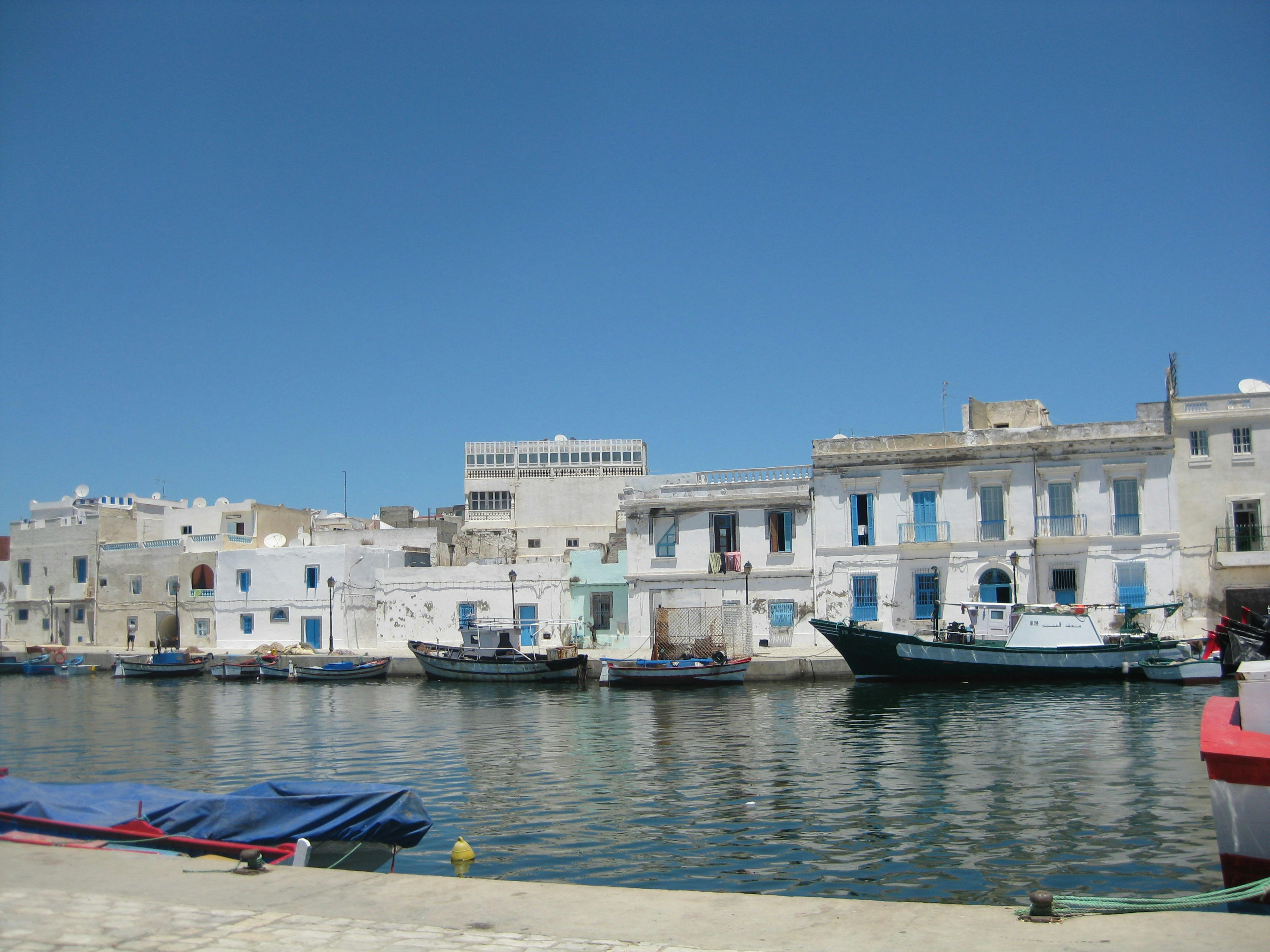 Vista escénica de edificios blancos a lo largo de un puerto tranquilo con cielo azul y barcos