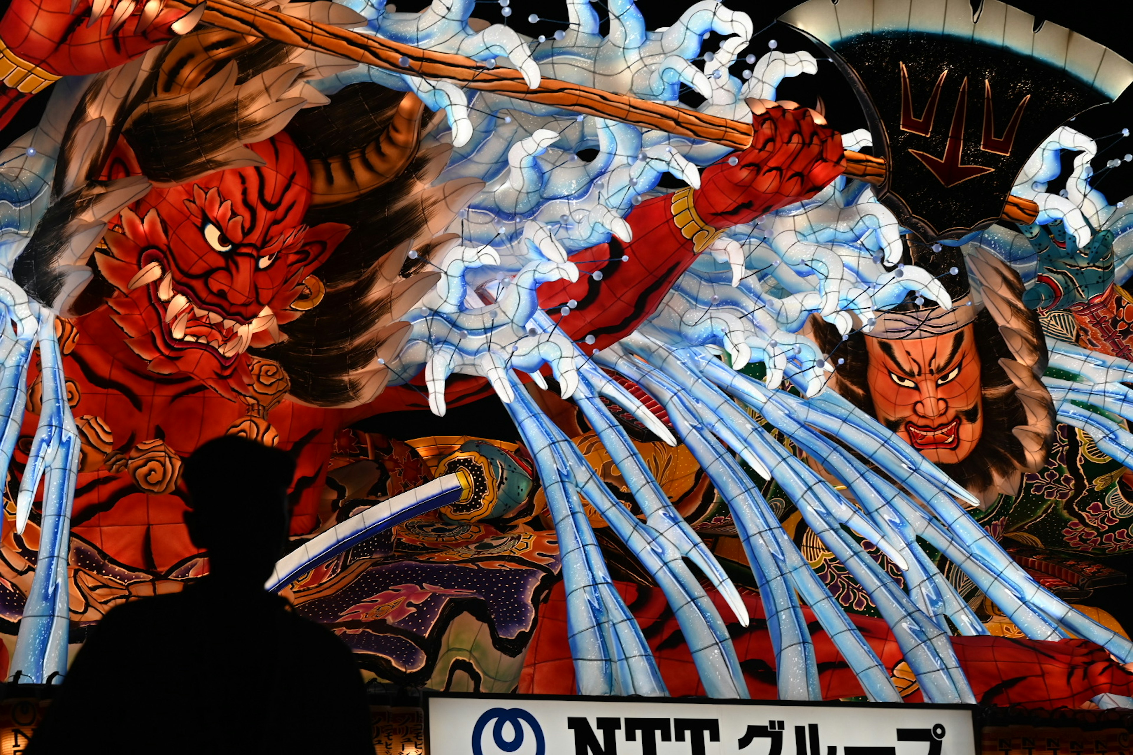 Silhouette of a person in front of a large mural depicting demons and waves