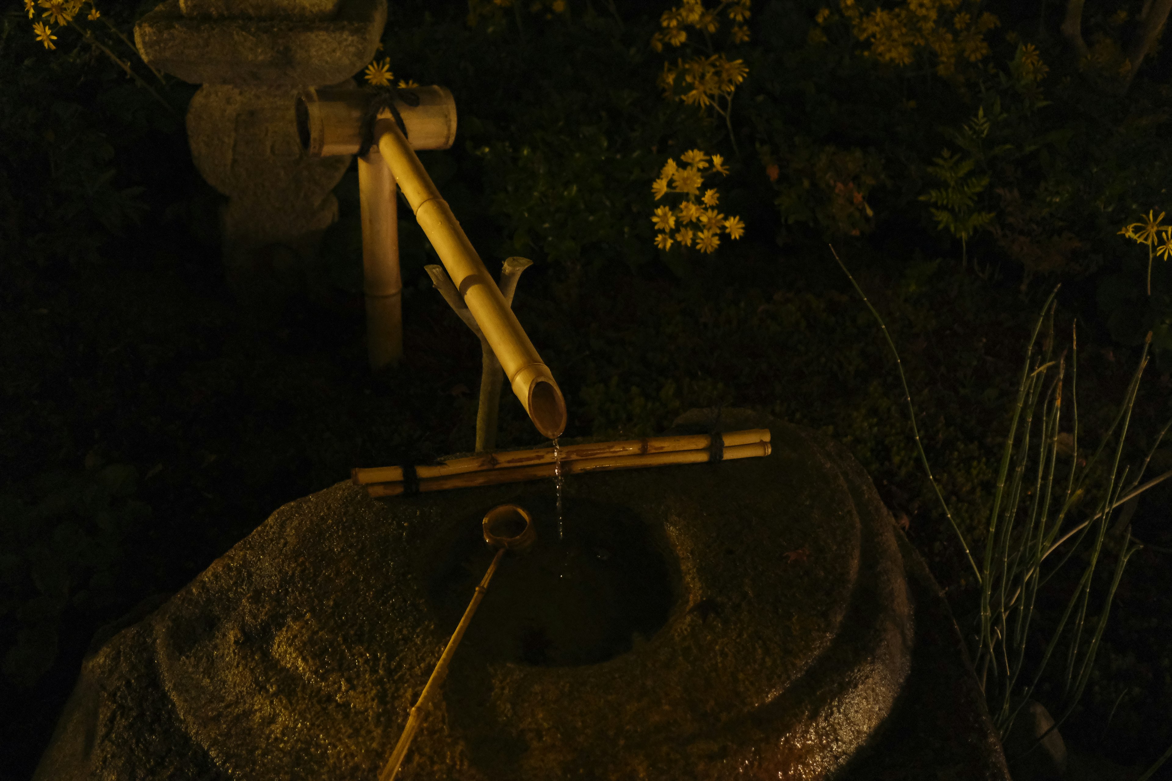 Bamboo water feature with flowing water over a stone basin at night