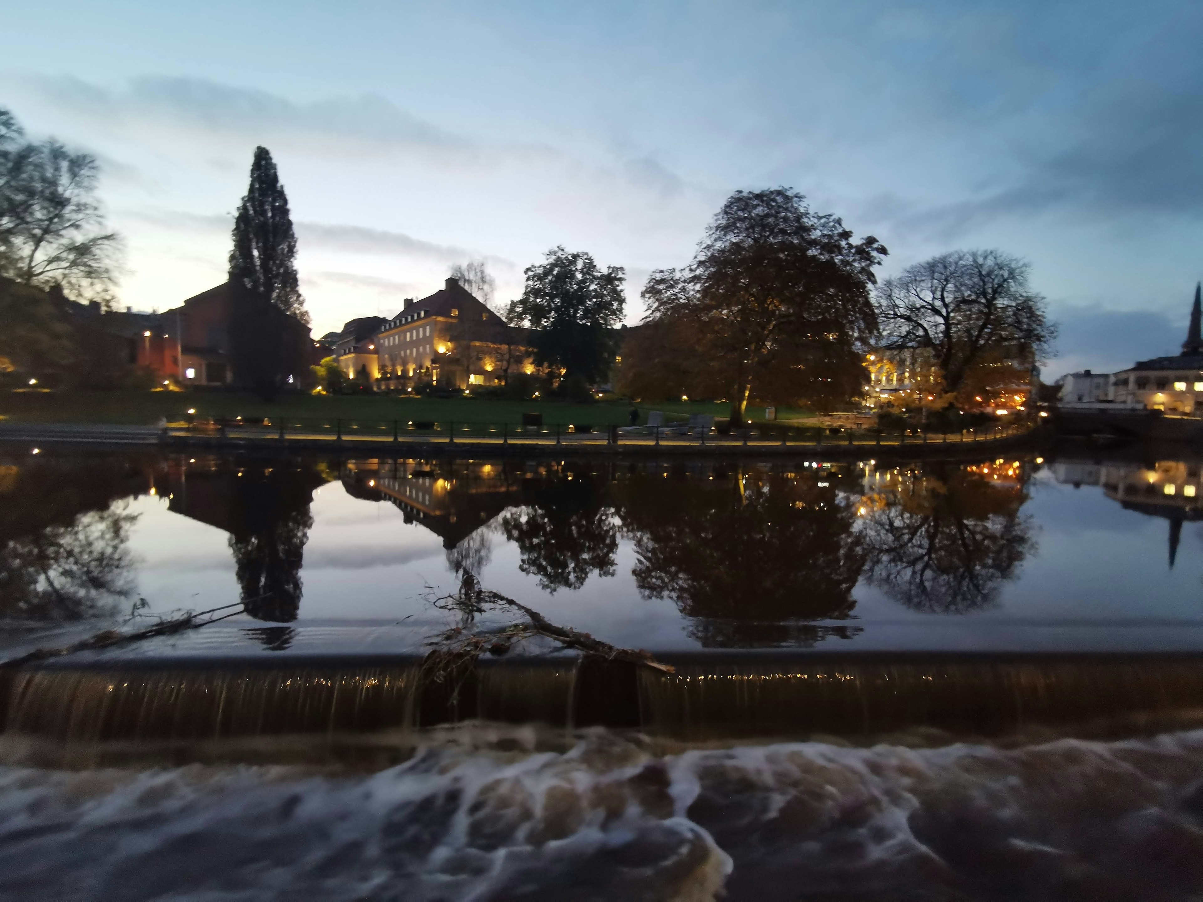 Escena de río al atardecer con reflejos de edificios y árboles