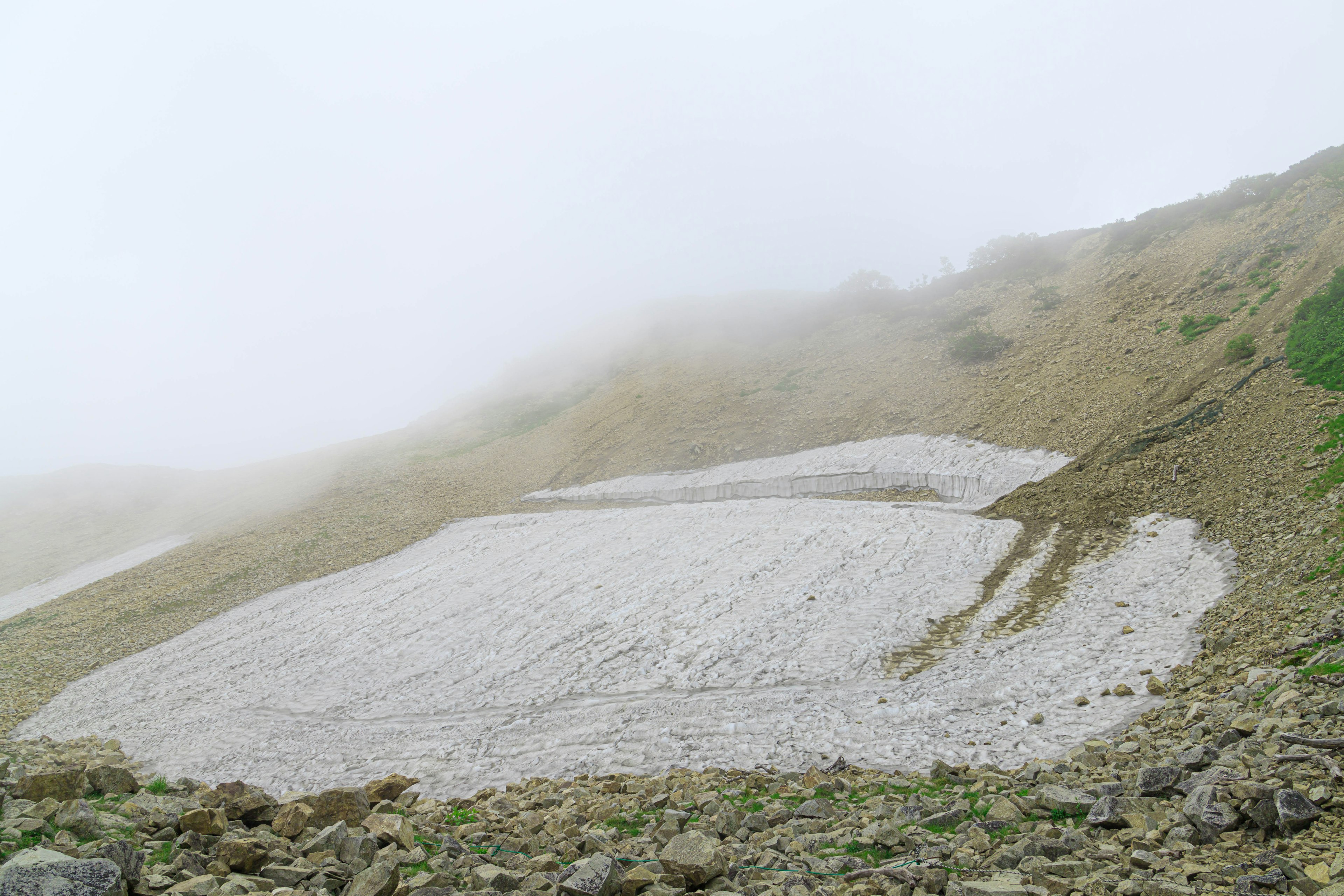 霧の中の山の斜面に広がる雪の残り