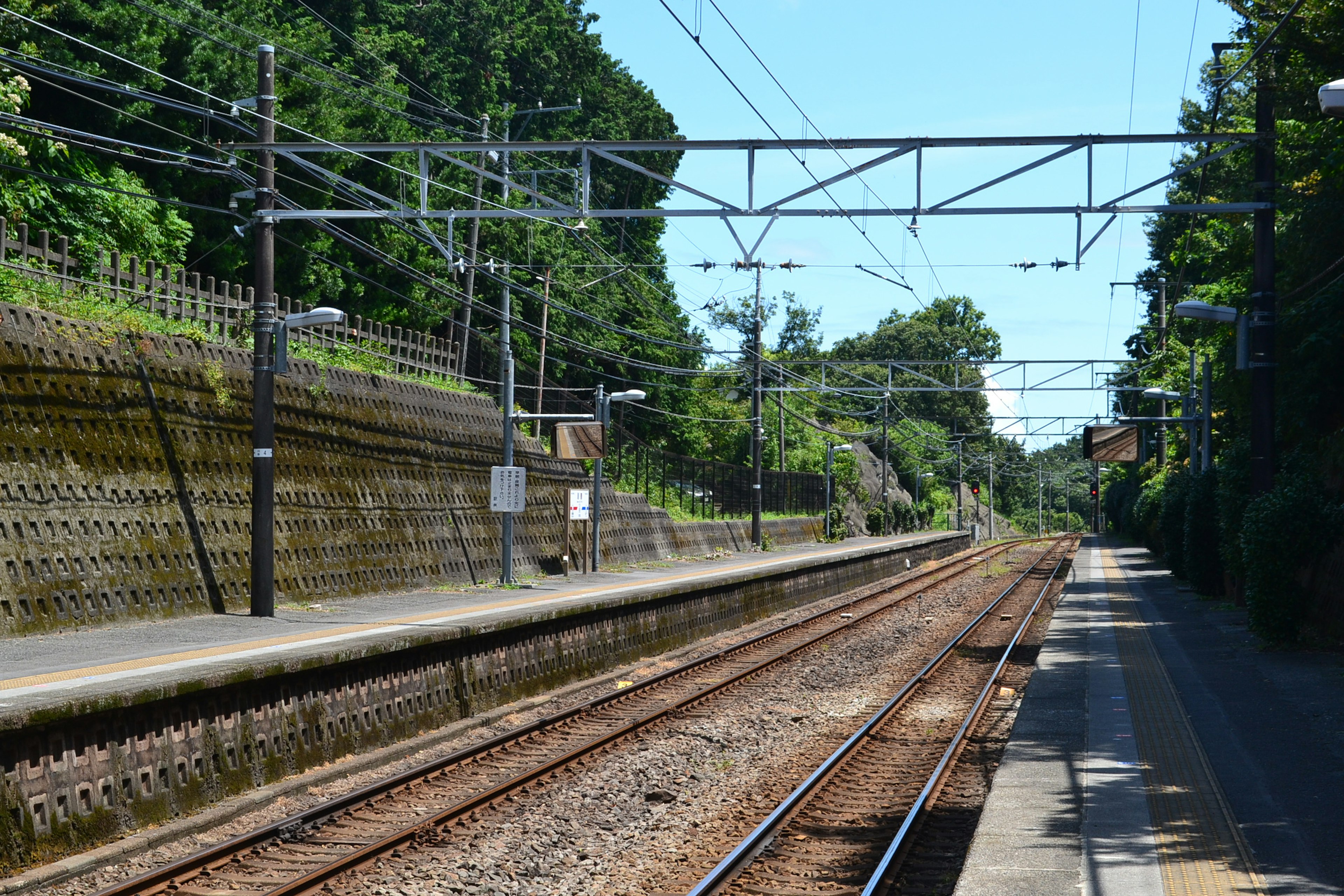 Quiet train station platform with visible tracks and greenery