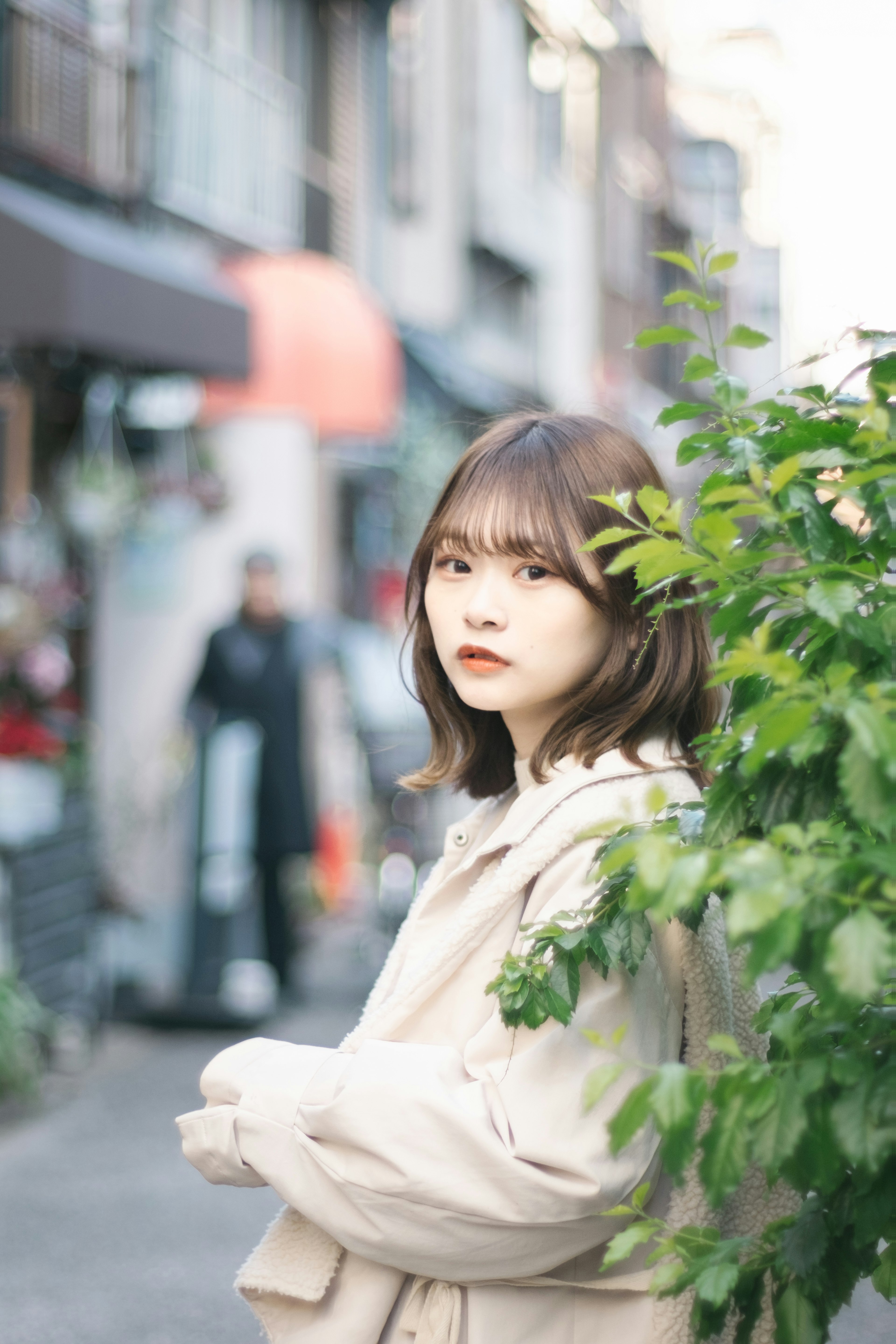 Portrait of a young woman partially hidden by green leaves in an urban setting