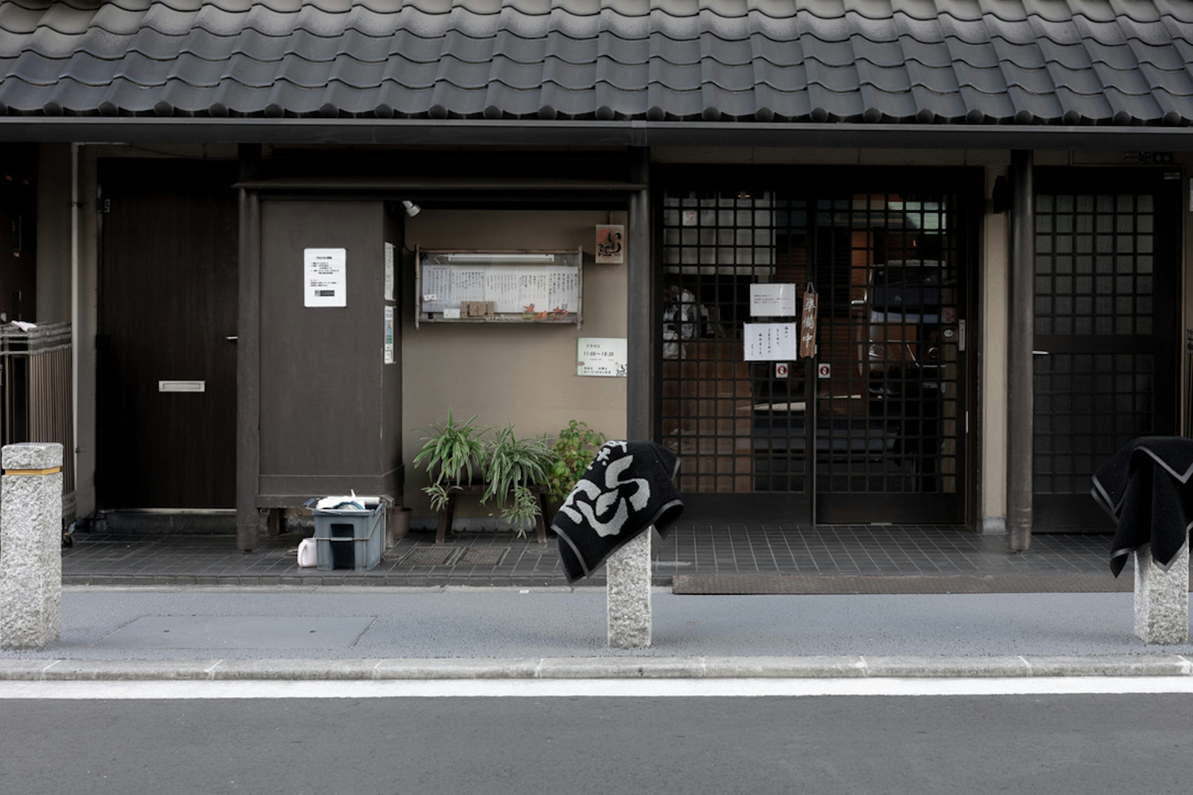 古い日本の家屋の外観、木製のドア、黒い瓦屋根、植物が置かれている