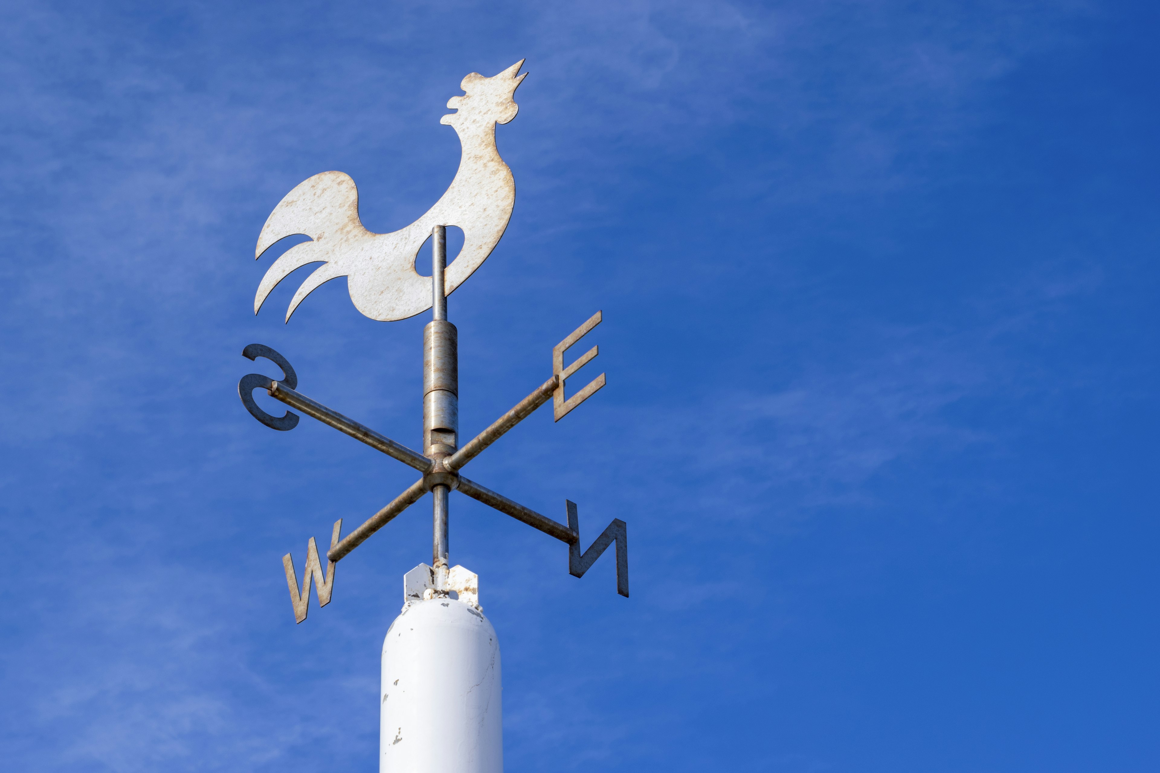 Metal weather vane featuring a rooster on a clear blue sky