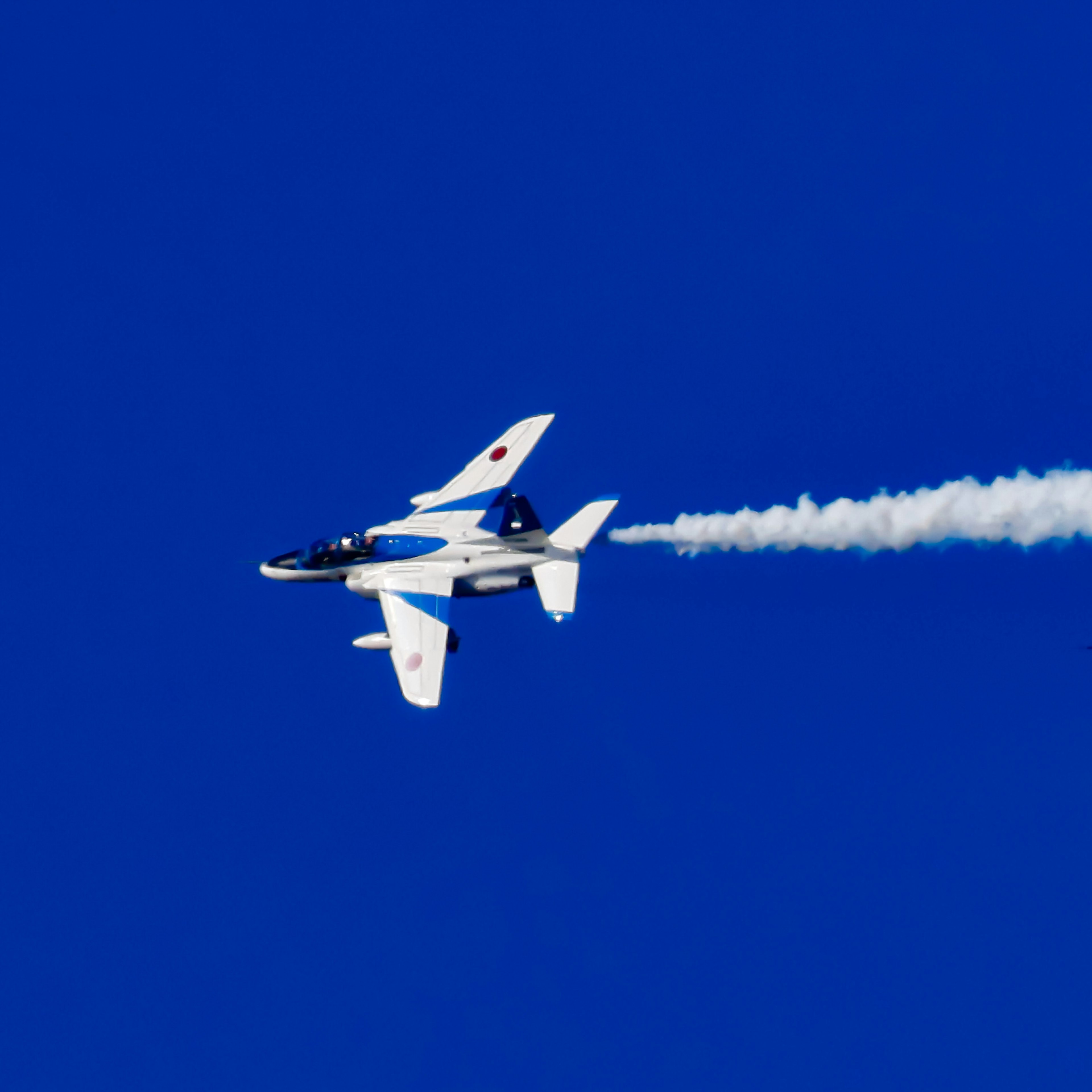 Un aereo da caccia bianco che vola contro un cielo blu lasciando una scia di fumo