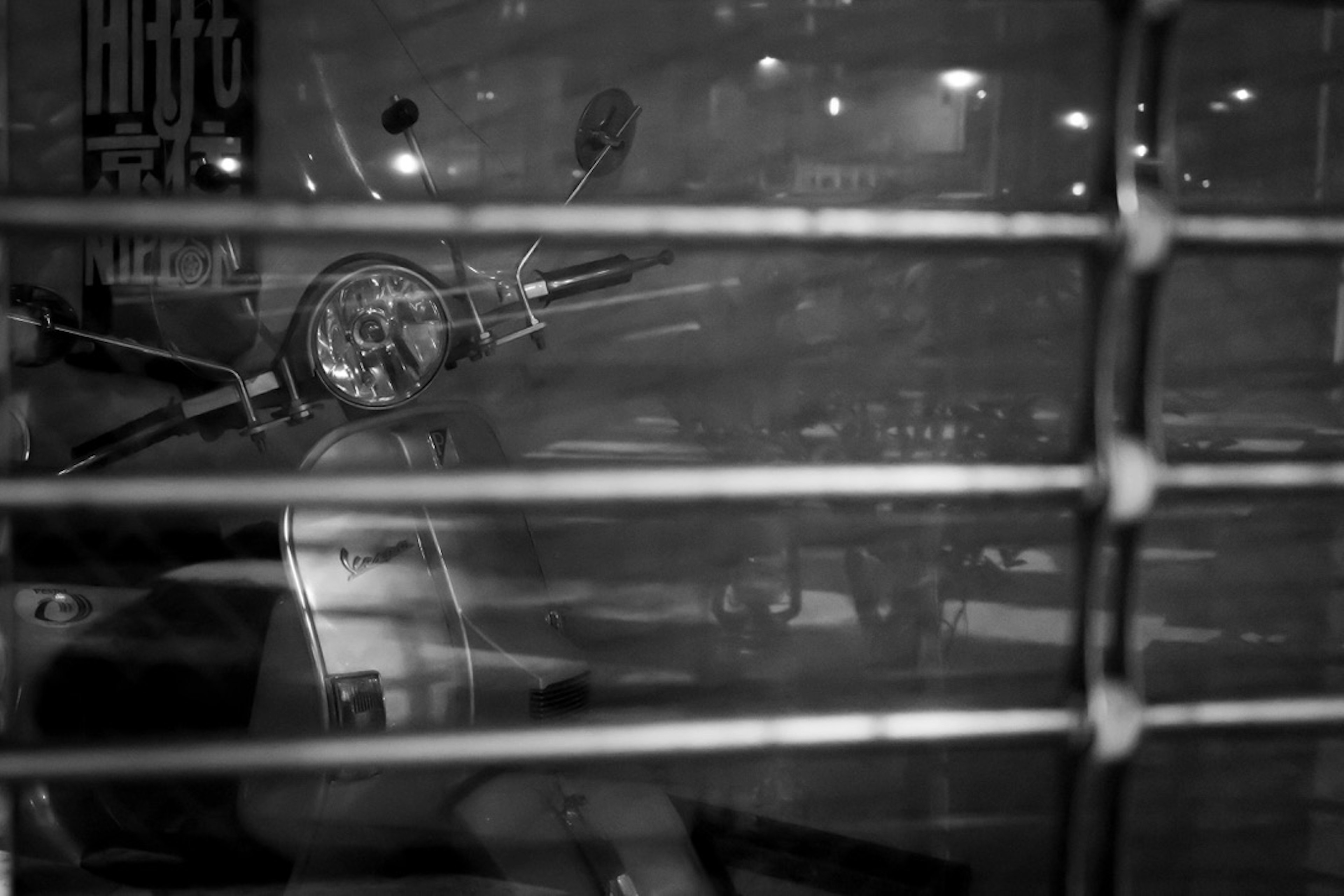 Black and white image of a motorcycle seen through bars in a night city scene