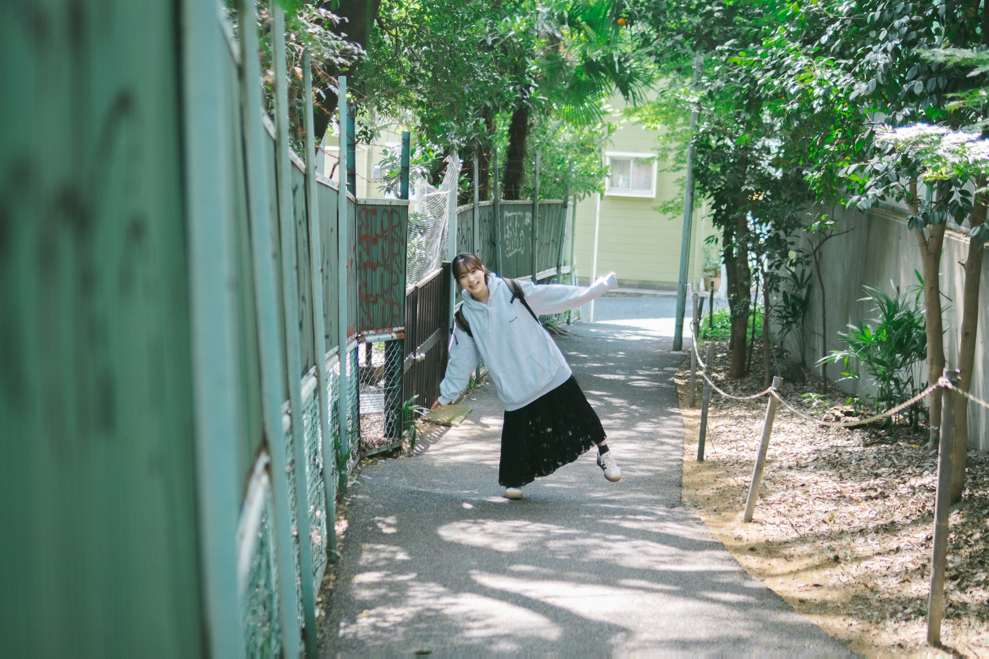 Girl posing on a tree-lined path with a green fence