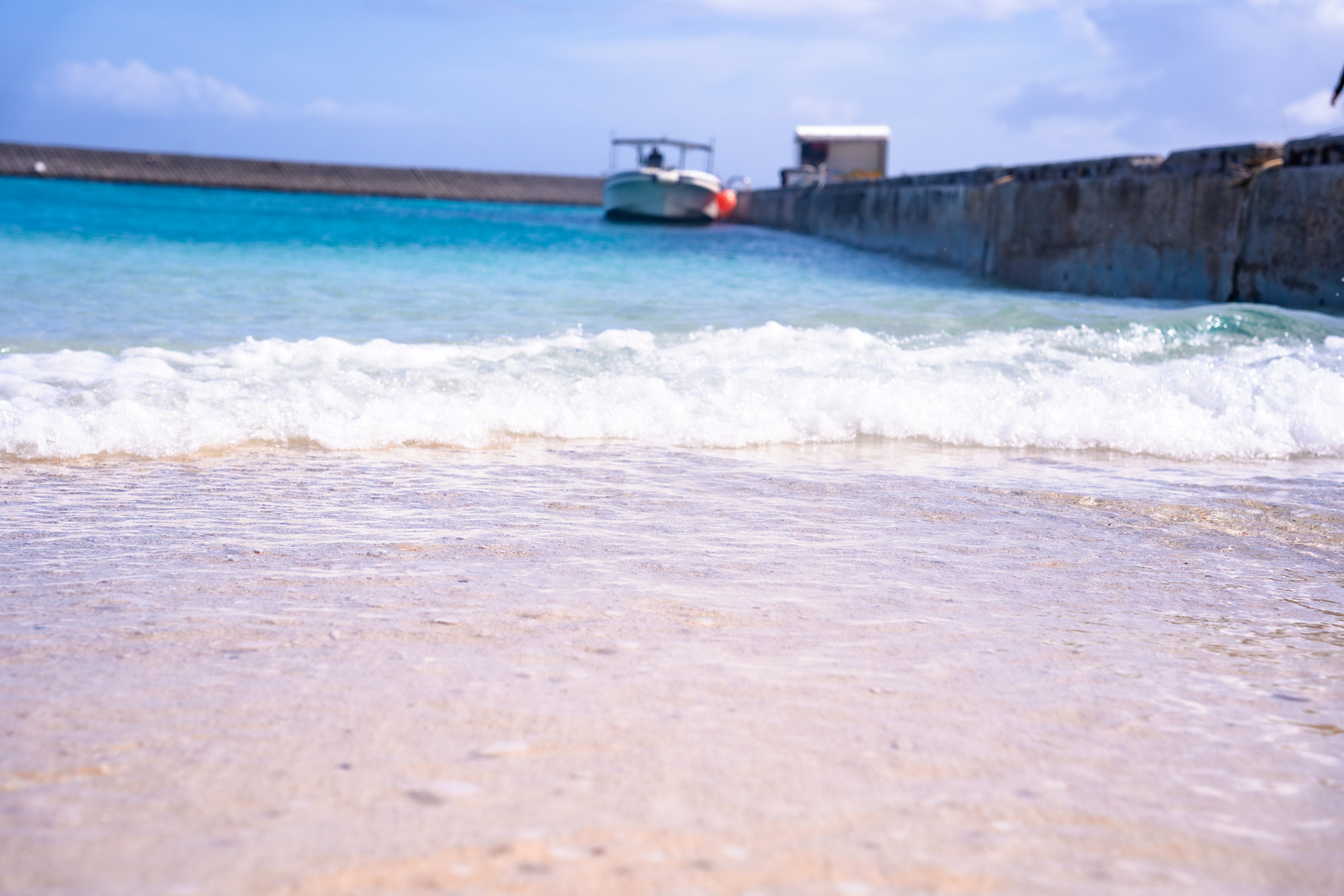 Scenic view of a beach with blue water and white waves featuring a boat and a pier