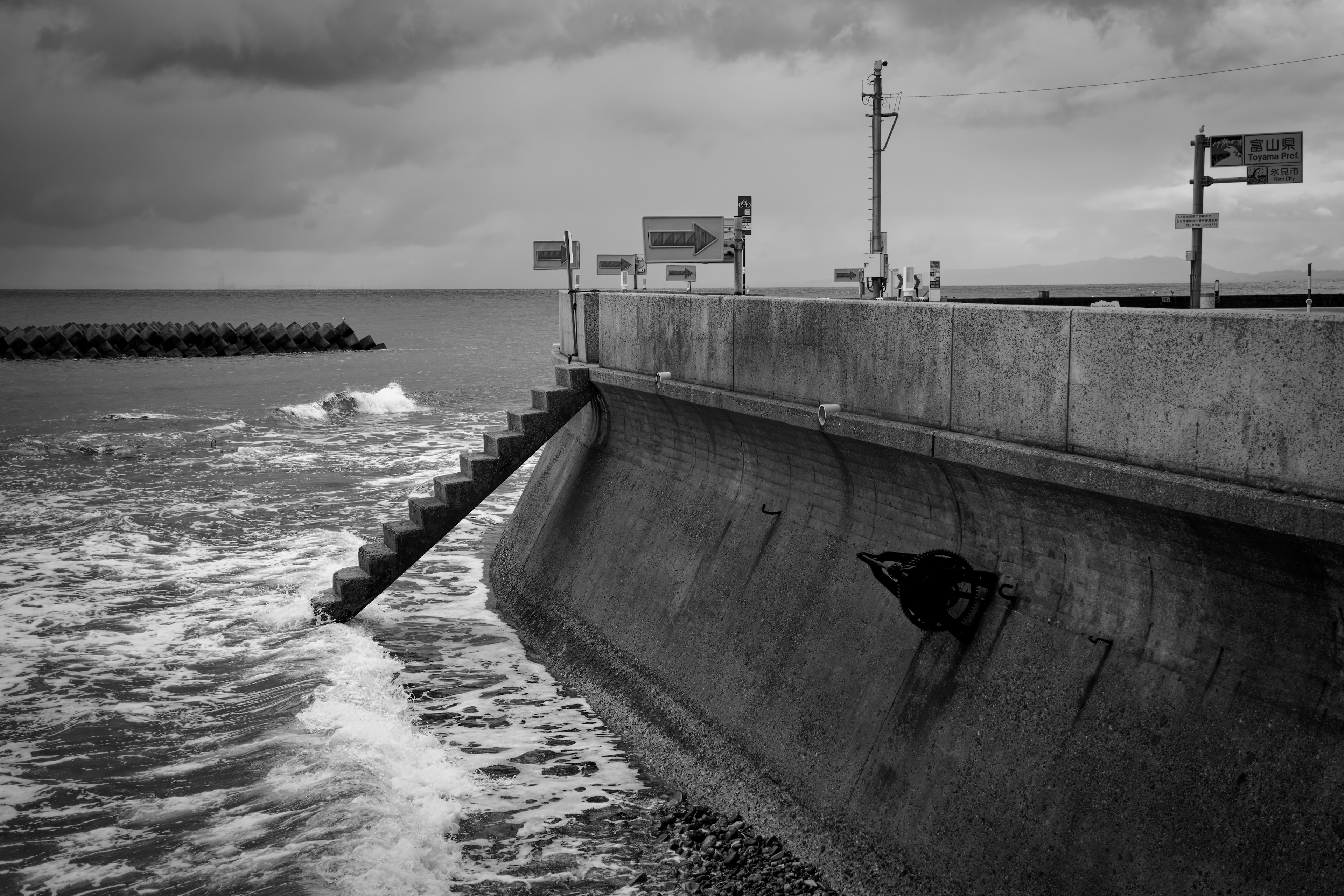 Vista en blanco y negro de un muro de mar de concreto con olas y cielo nublado