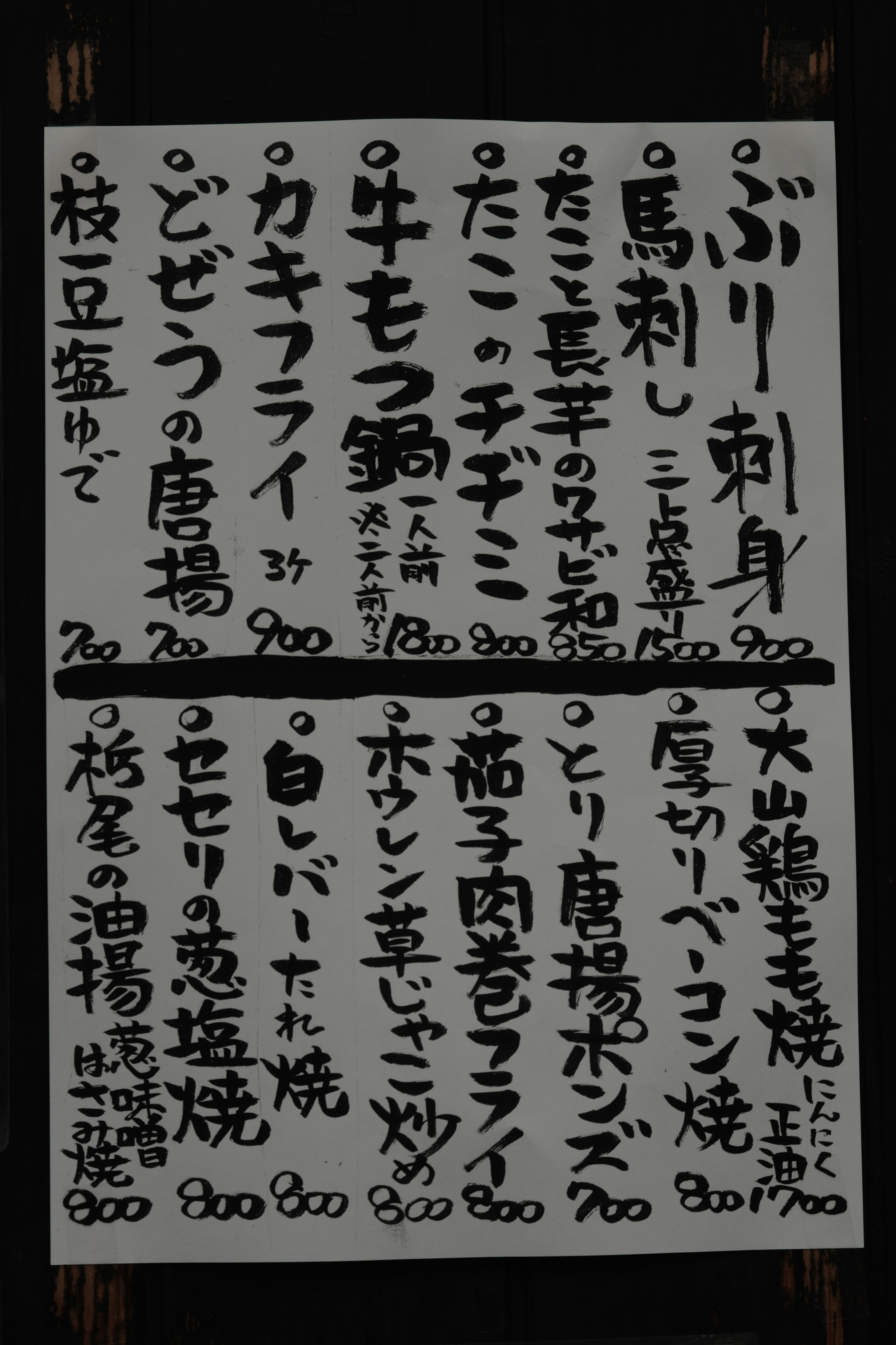 日本語のメニュー看板に手書きの料理名と価格が並ぶ