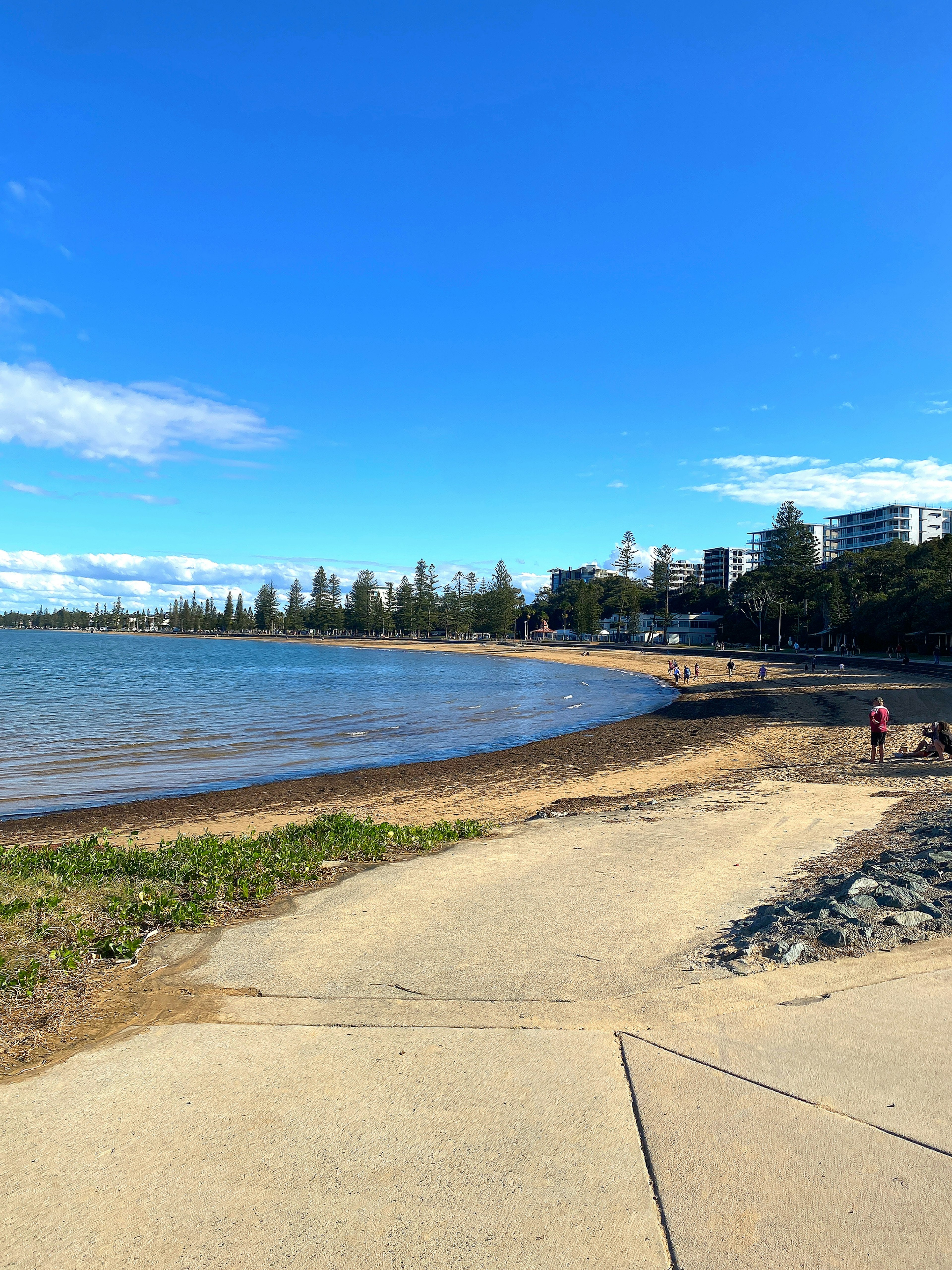 Vista escénica de playa con cielo azul claro y personas caminando