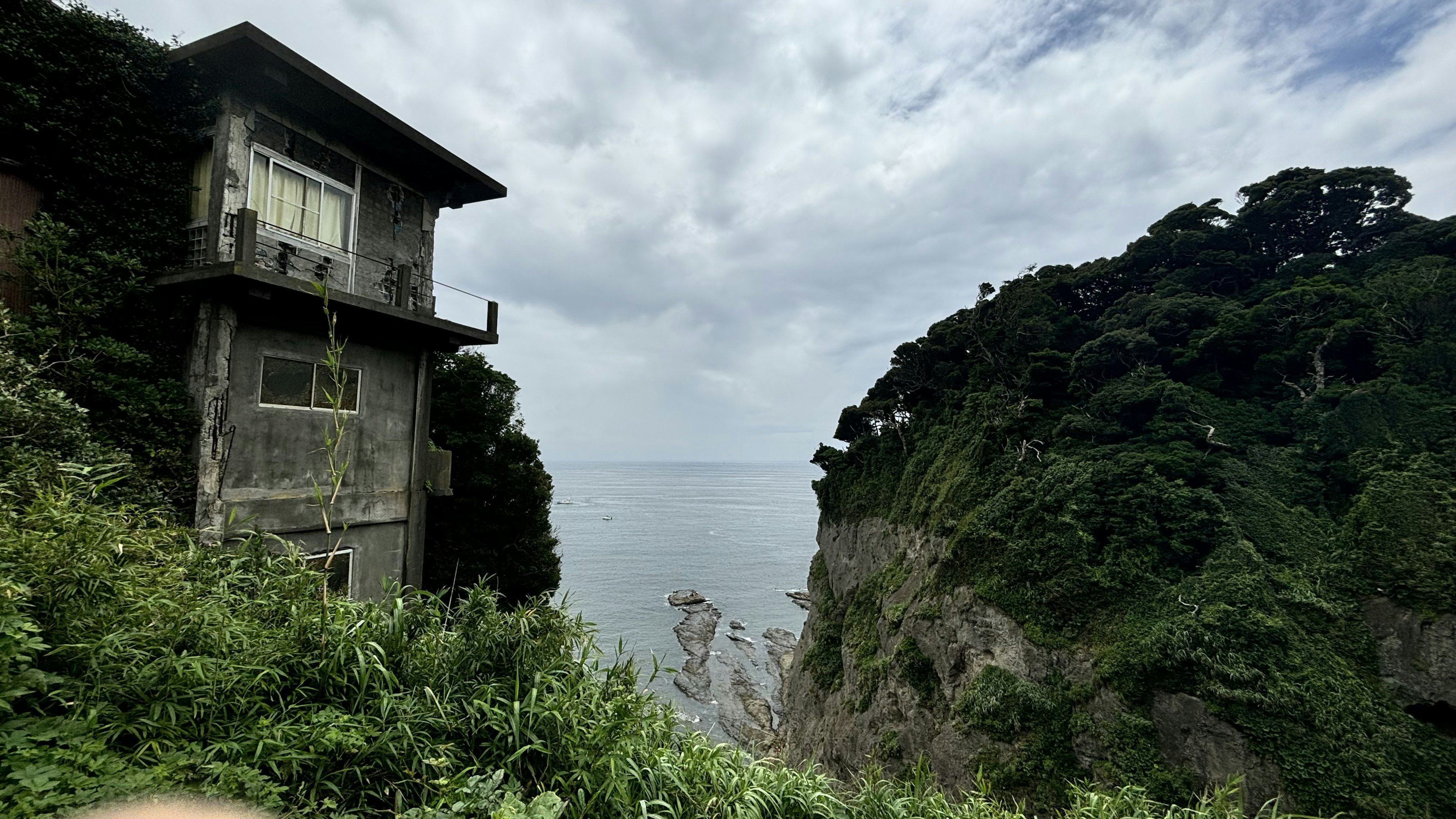 Verlassenes Gebäude mit Blick auf das Meer und üppiger Vegetation an den Klippen