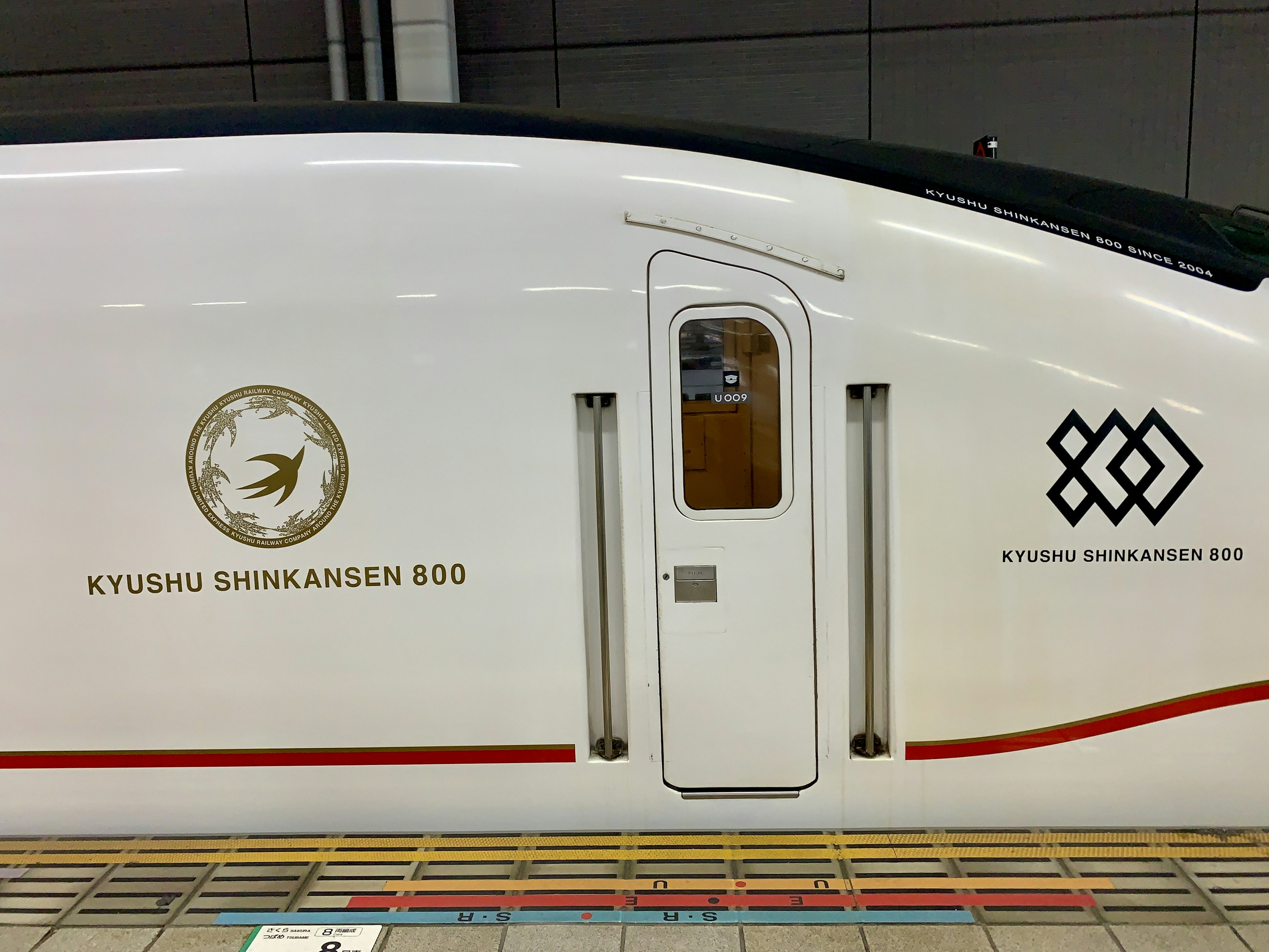 Seitenansicht eines weißen Kyushu Shinkansen-Zuges mit Logos und einer Tür