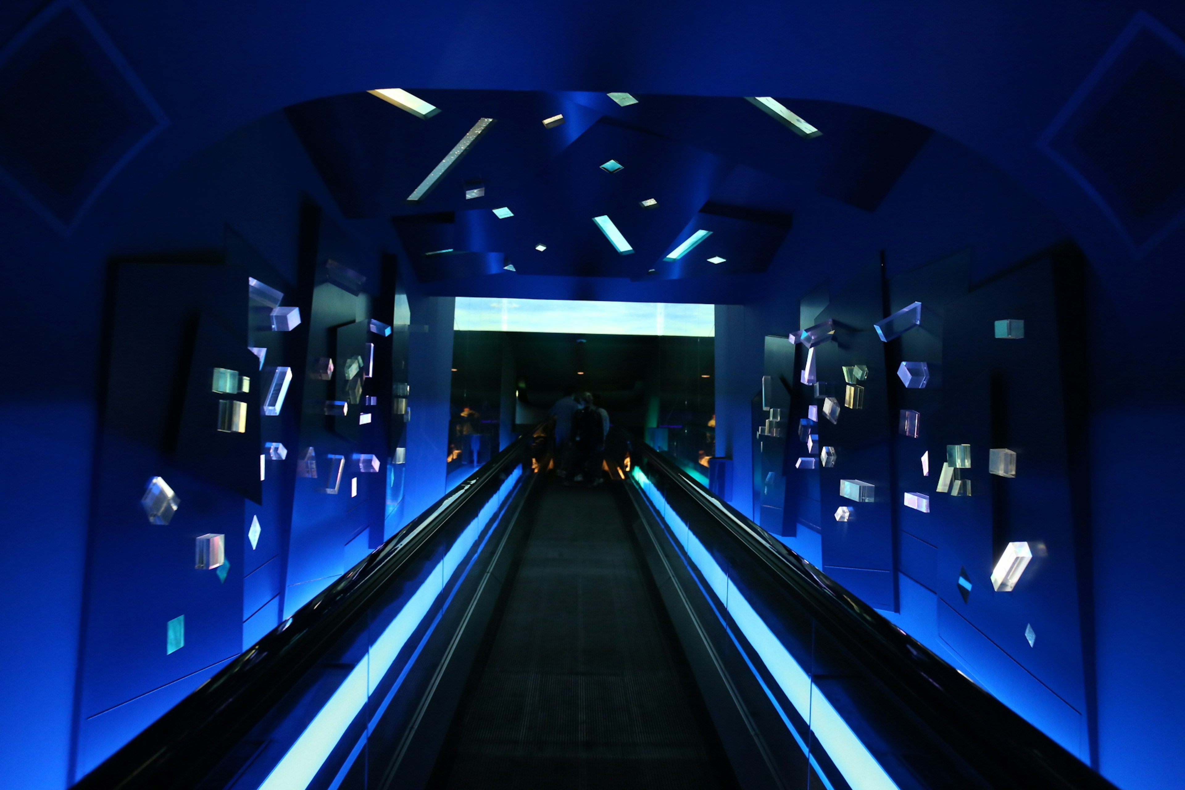 Interior de un túnel futurista con iluminación azul y pasillo móvil