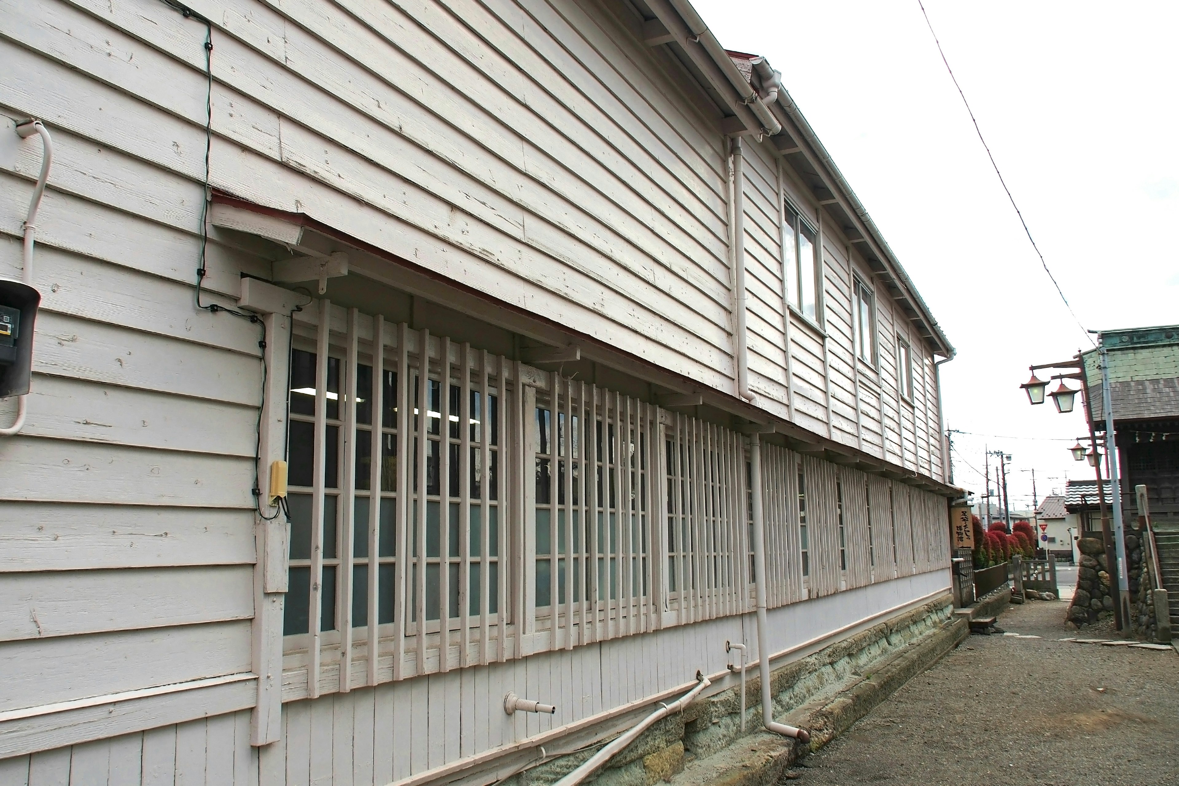 Extérieur d'un bâtiment en bois blanc avec des fenêtres barrées donnant sur la rue