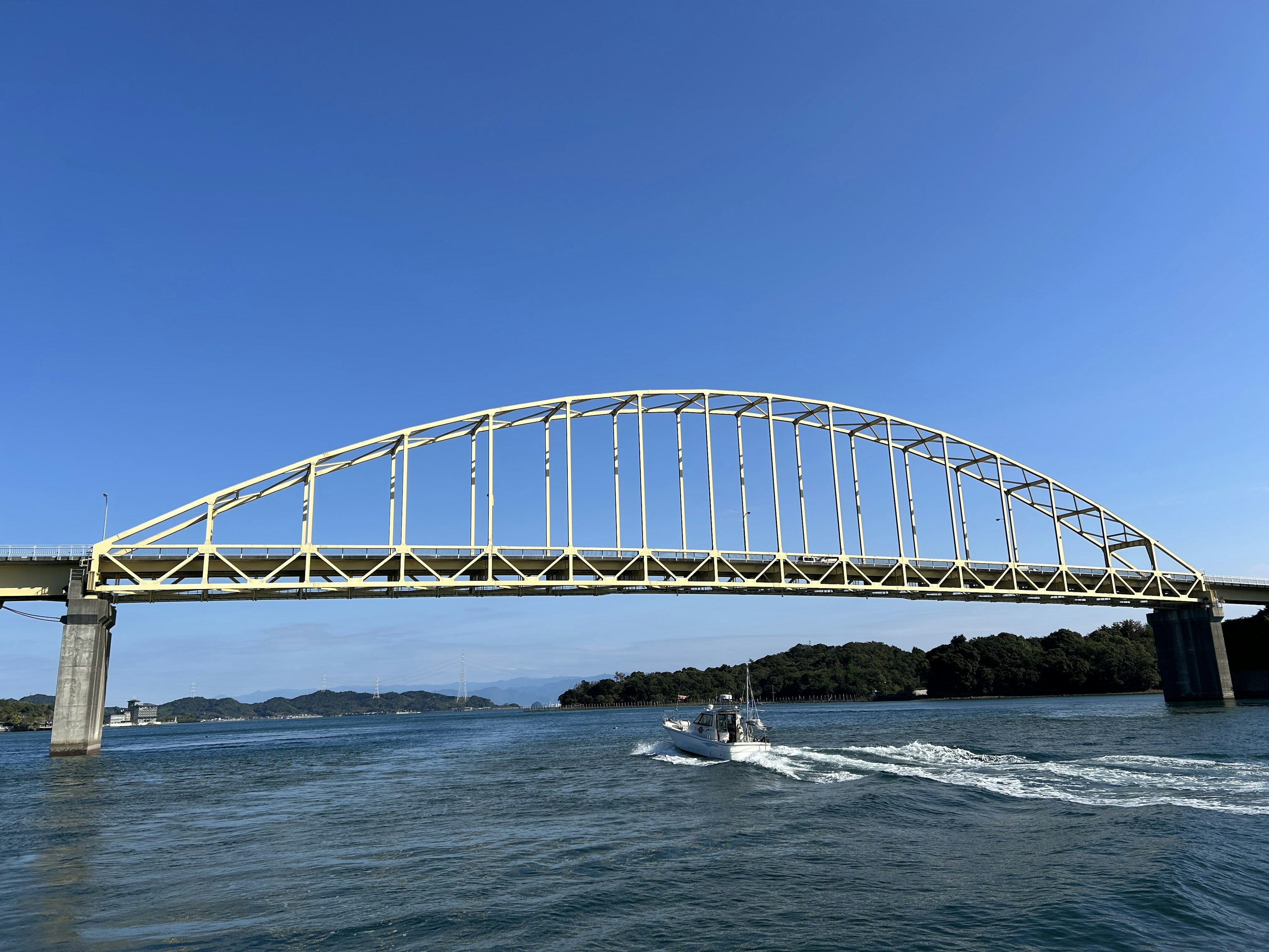 Pont en arc jaune sous un ciel bleu avec un bateau passant en dessous