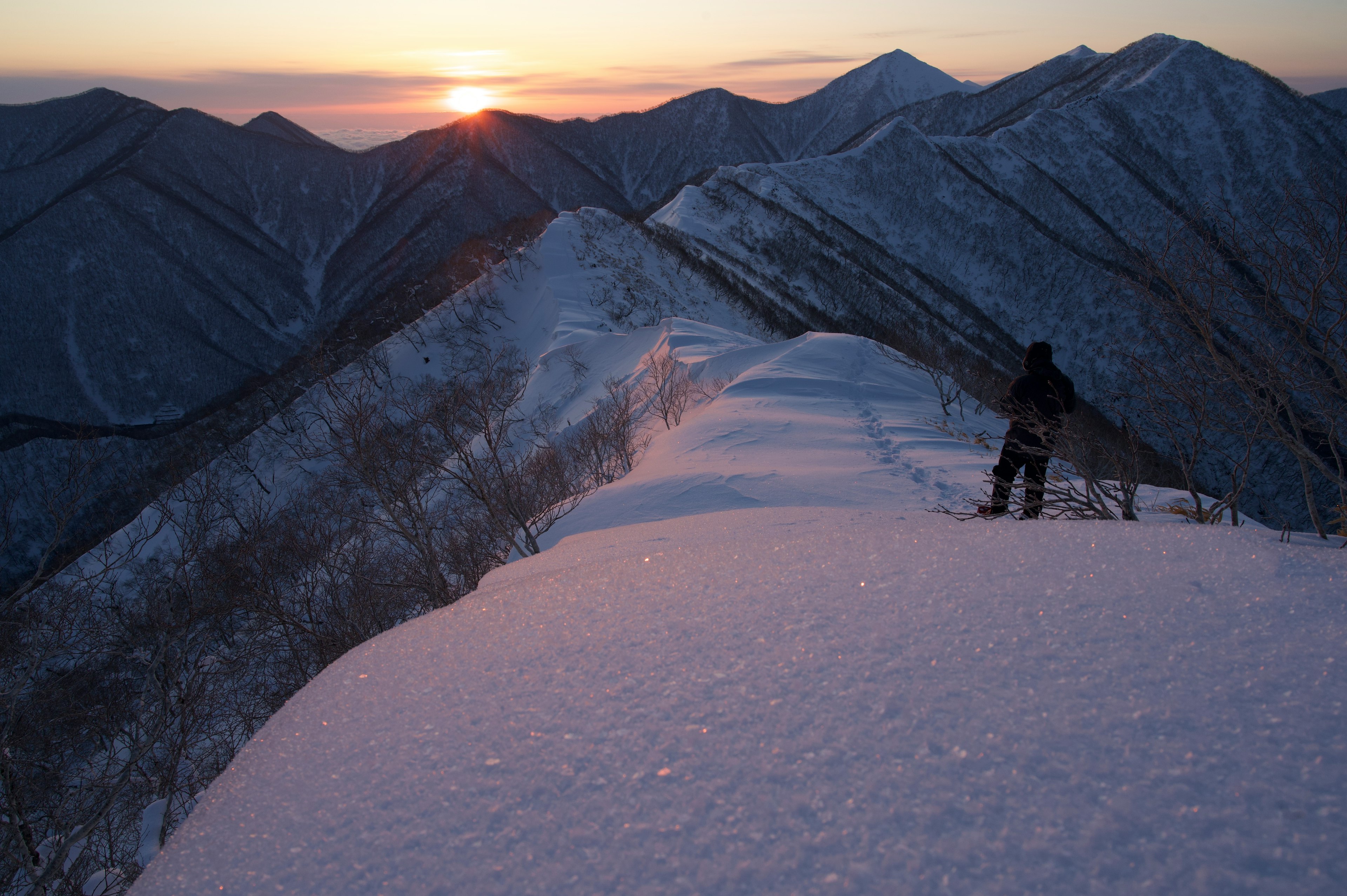 Persona che osserva una cresta montuosa innevata al tramonto