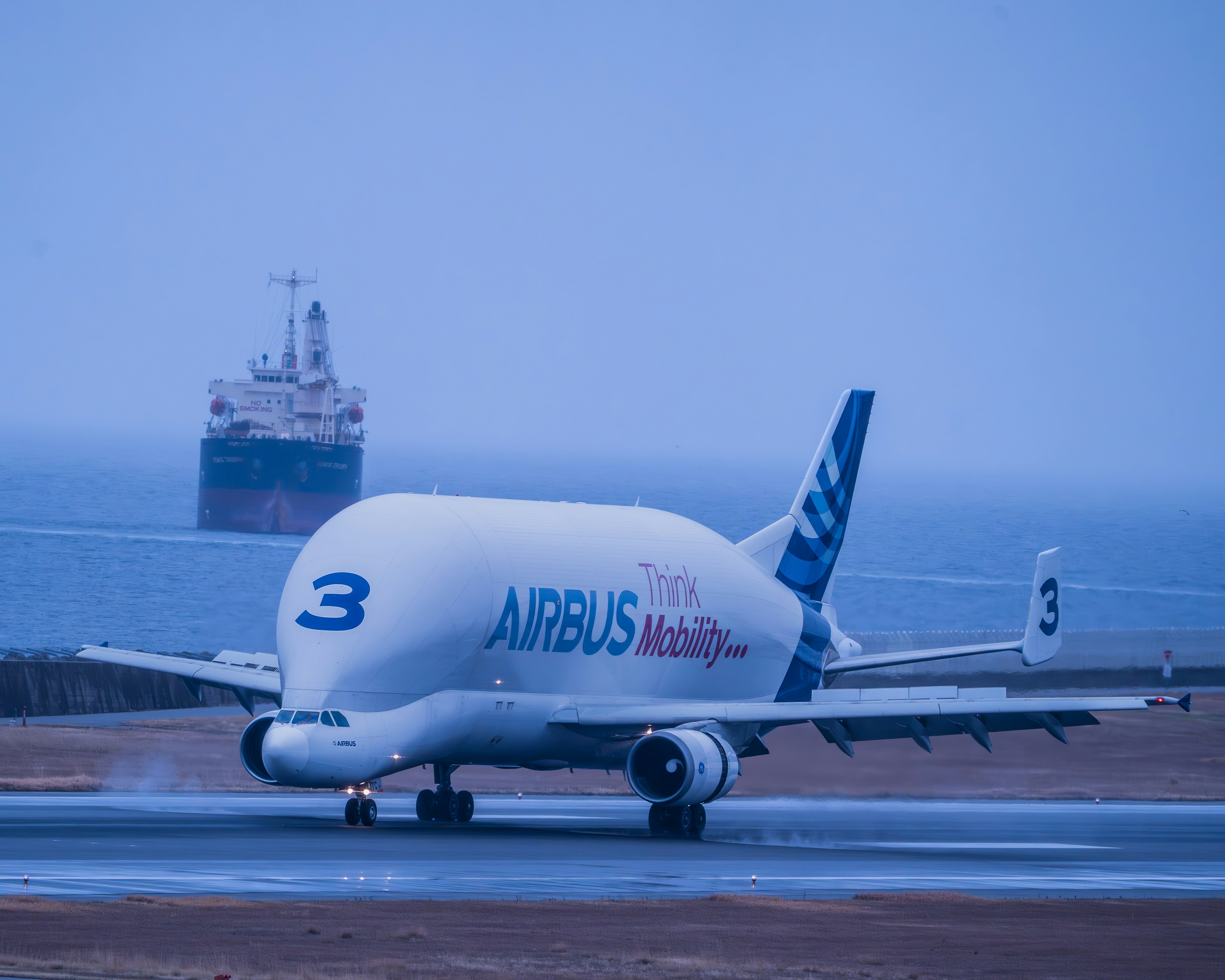 Pesawat kargo Airbus meluncur di landasan dengan laut dan kapal di latar belakang