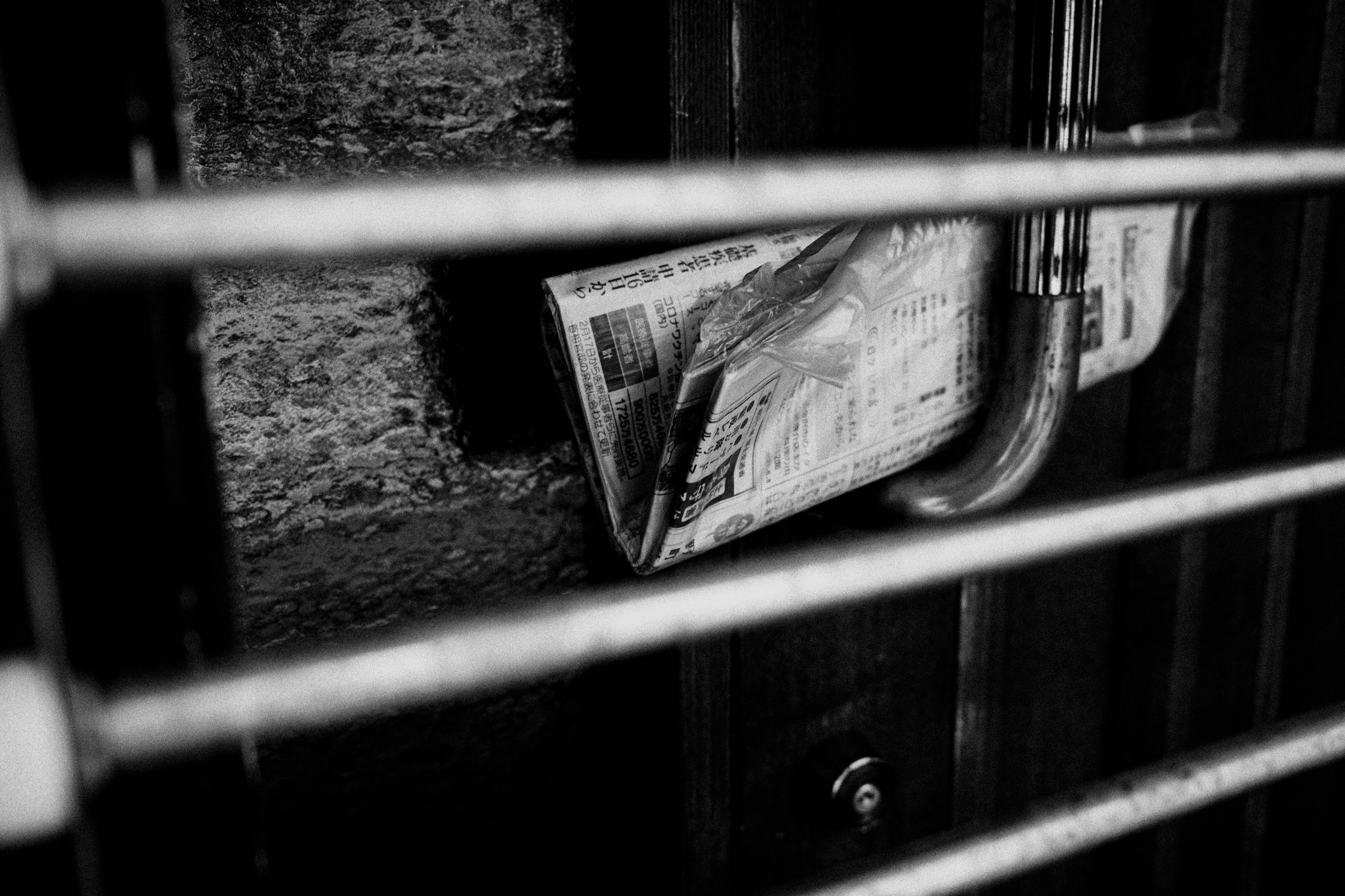 Black and white photo showing a bundle of newspapers visible through bars