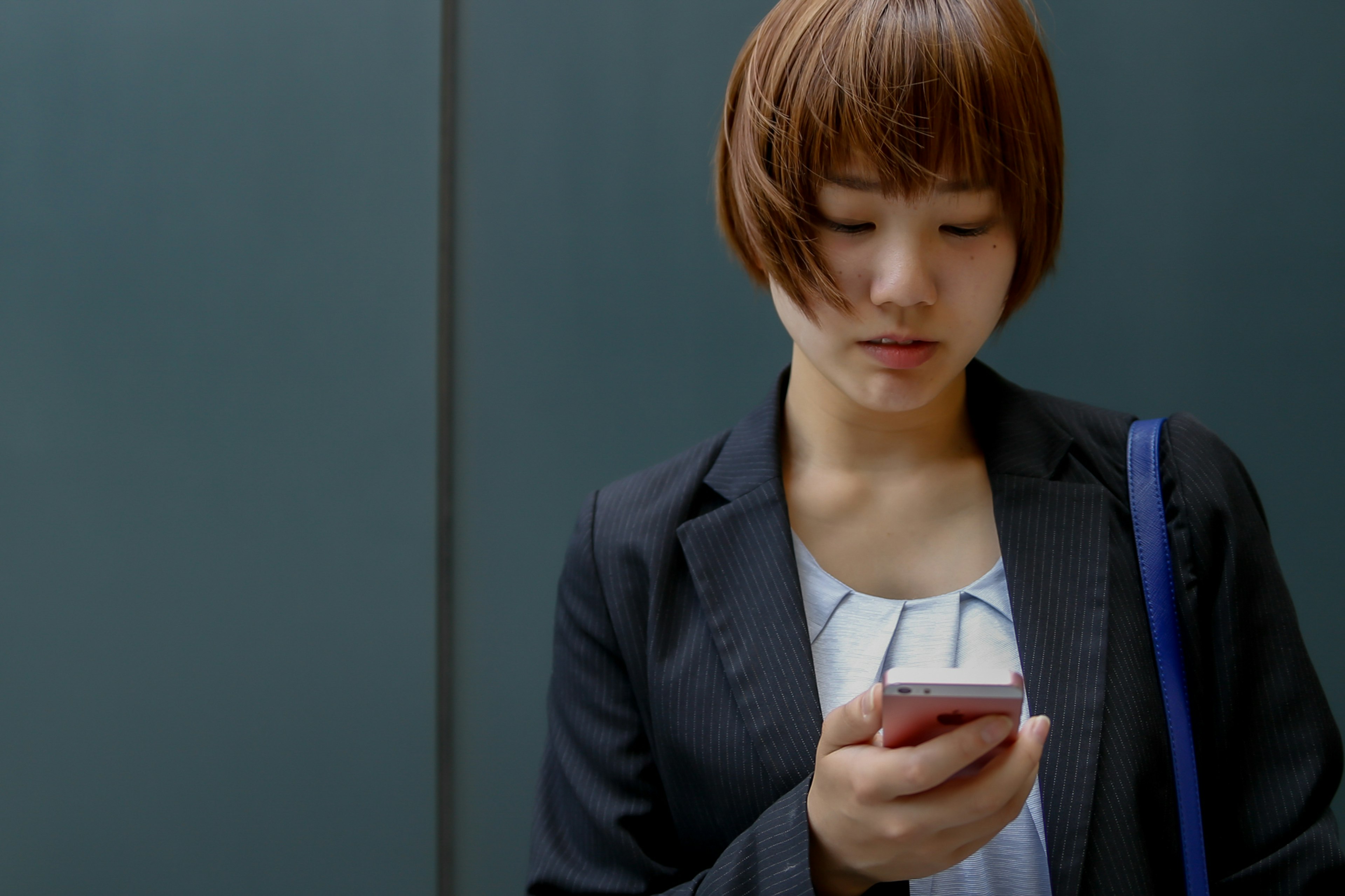 Frau mit kurzen Haaren, die auf ihr Smartphone in business-casual Kleidung schaut