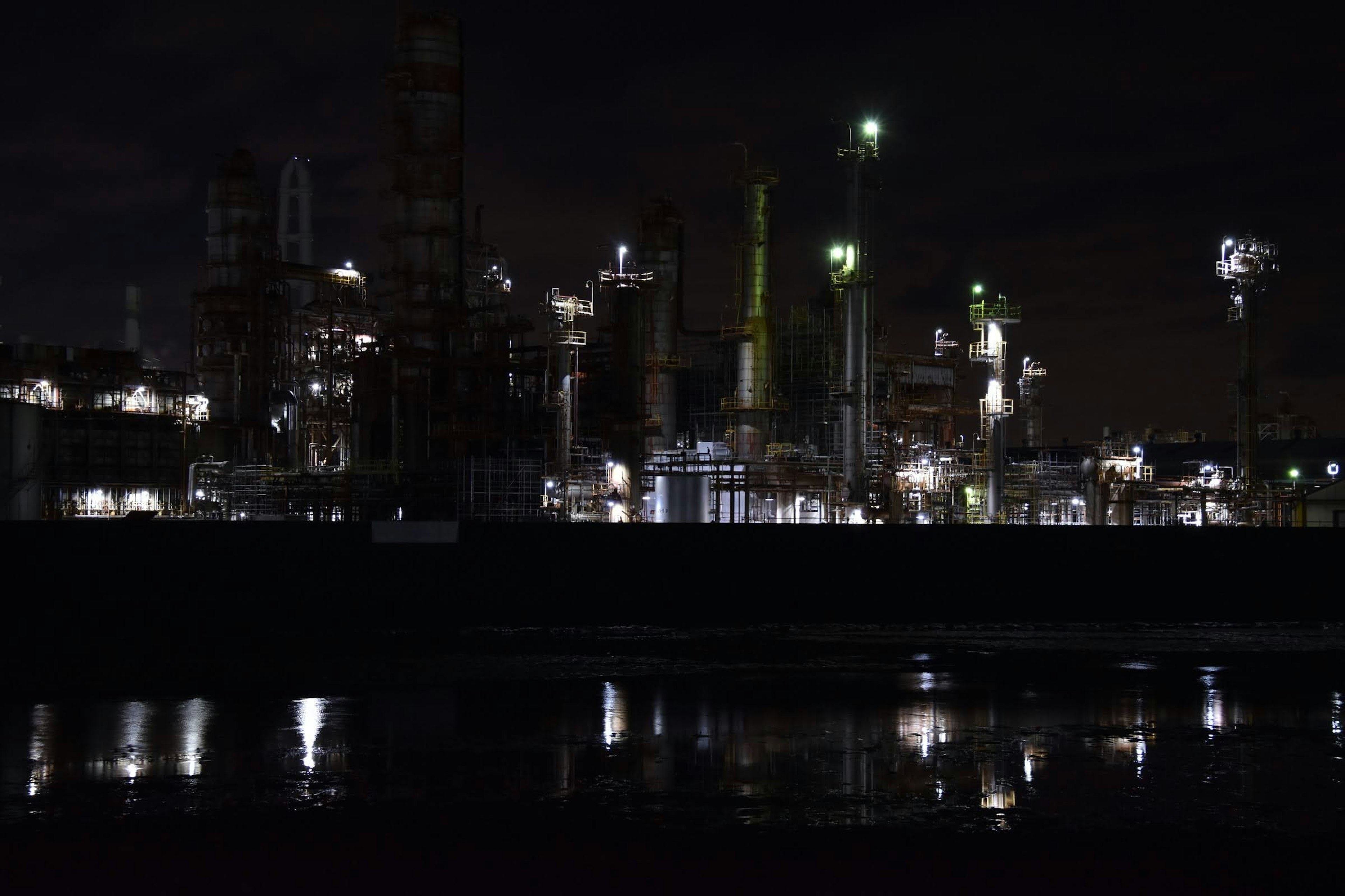 Vista nocturna de una planta industrial iluminada con reflejos en el agua