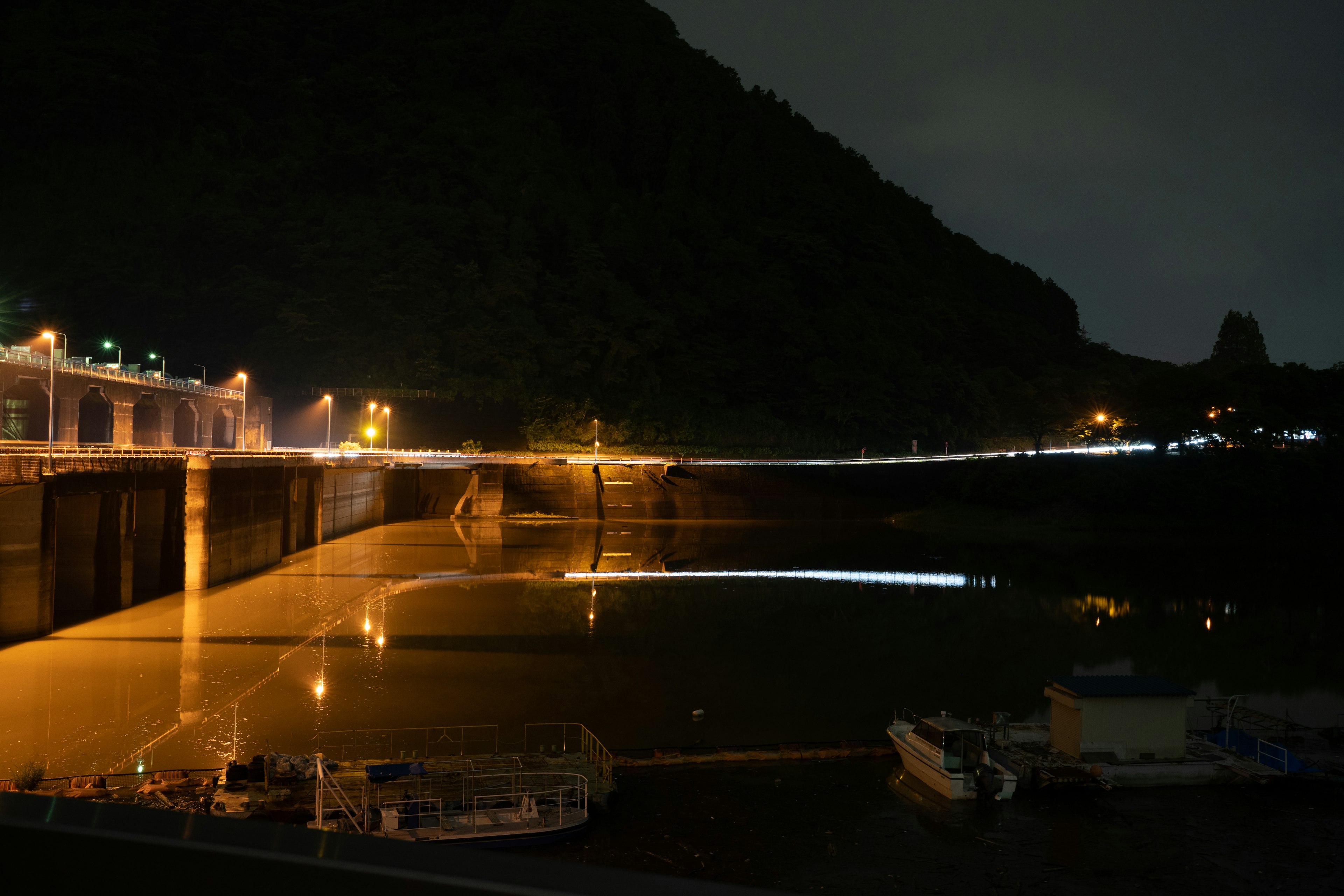 Vista nocturna de un puerto con barcos y silueta de montaña