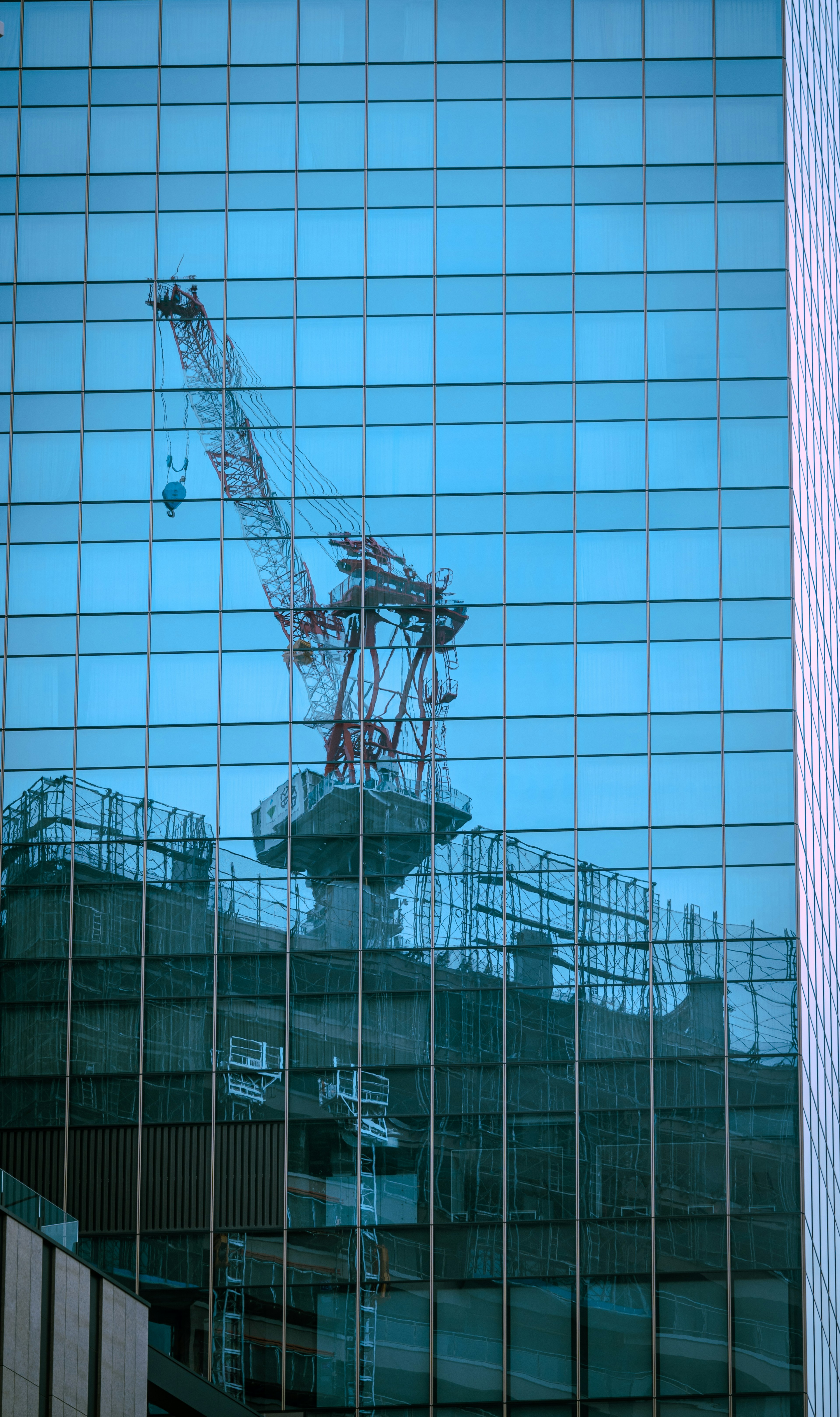 Grúa y sitio de construcción reflejados en un edificio de vidrio azul