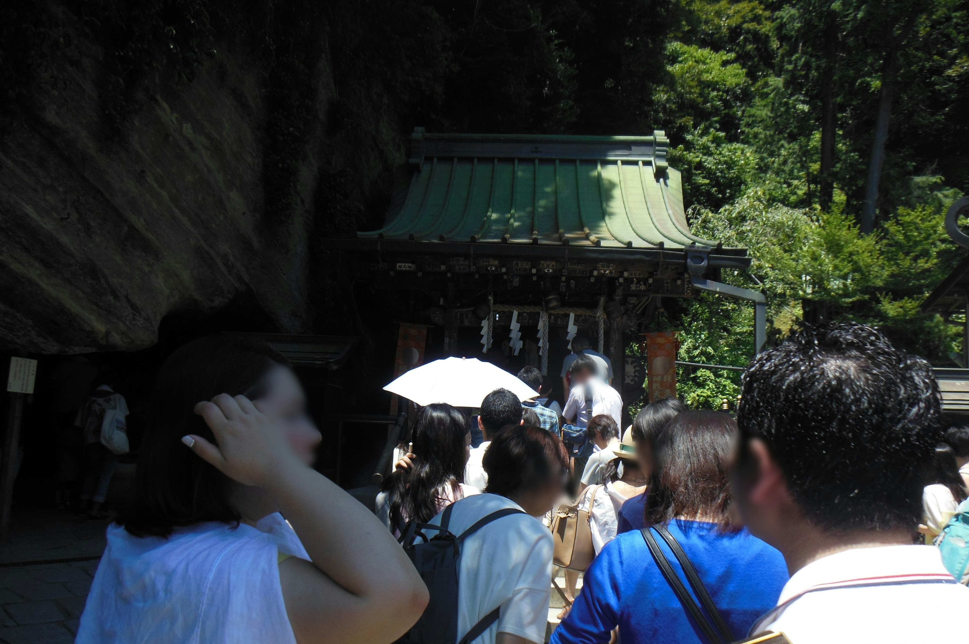 Foule rassemblée près d'un sanctuaire avec un toit vert entouré de nature