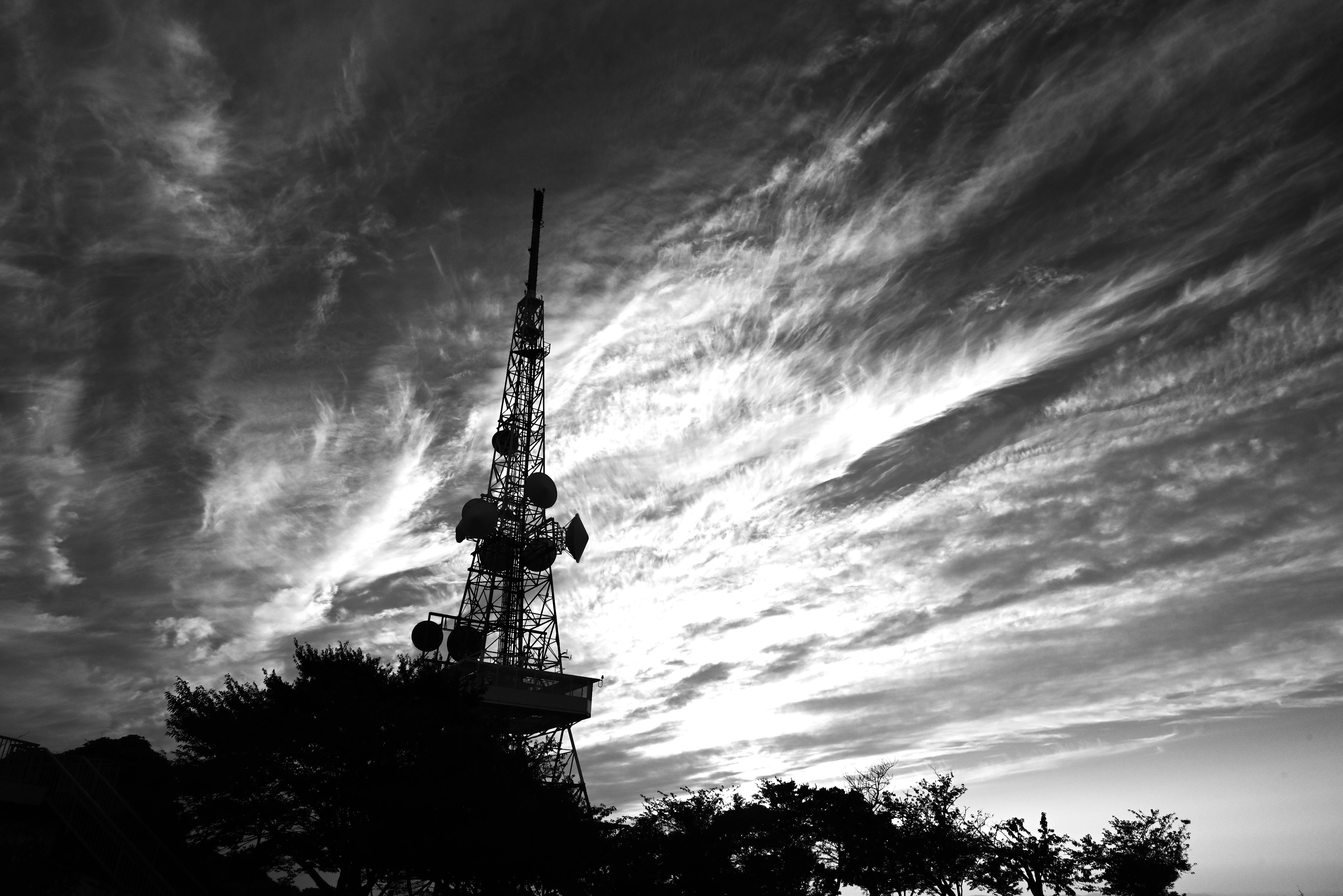 Silhouette di una torre di comunicazione contro un cielo drammatico in bianco e nero